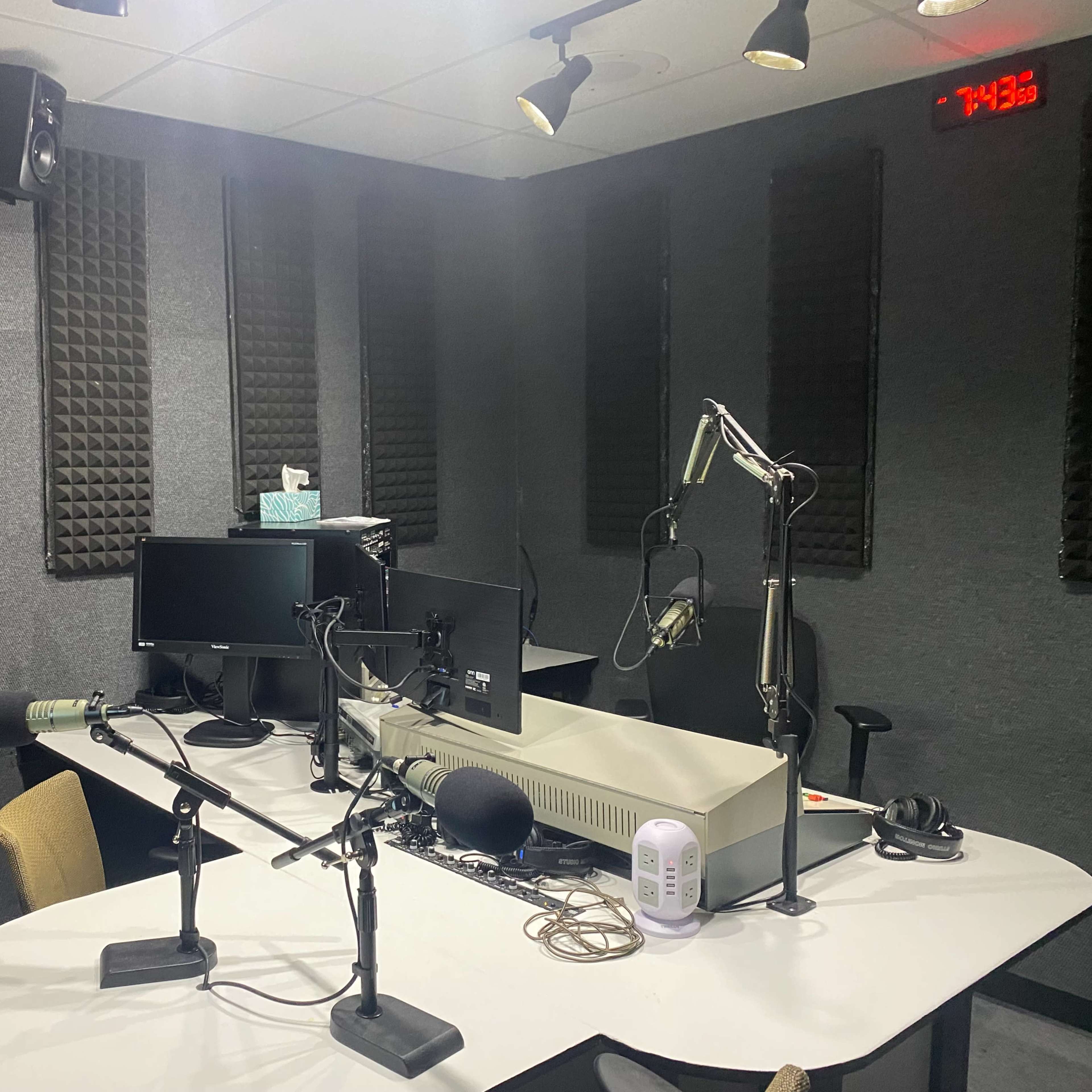 A soundproof recording studio with a central table, microphones, and computer monitors.