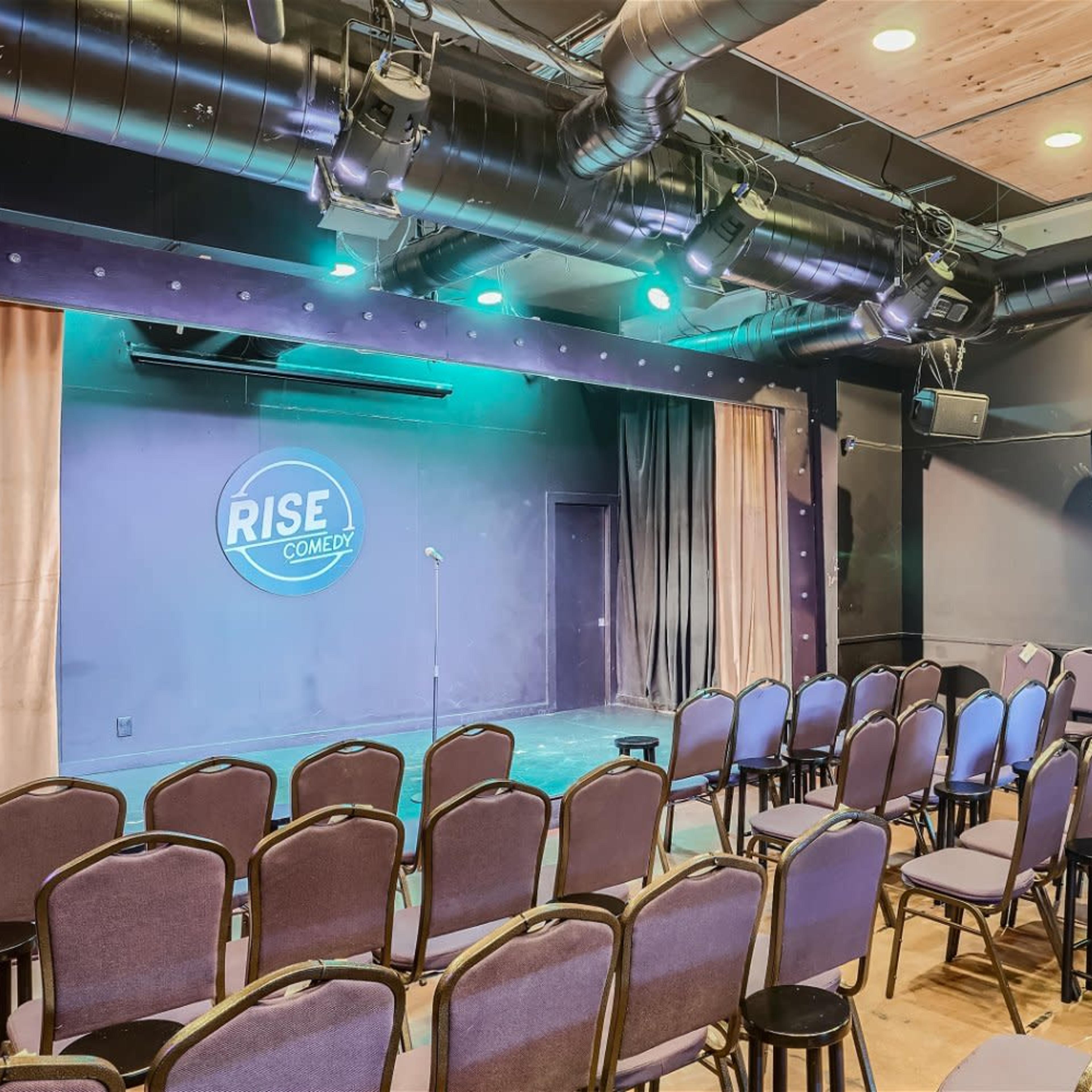 A comedy stage with a microphone stand, surrounded by neatly arranged chairs facing the stage.