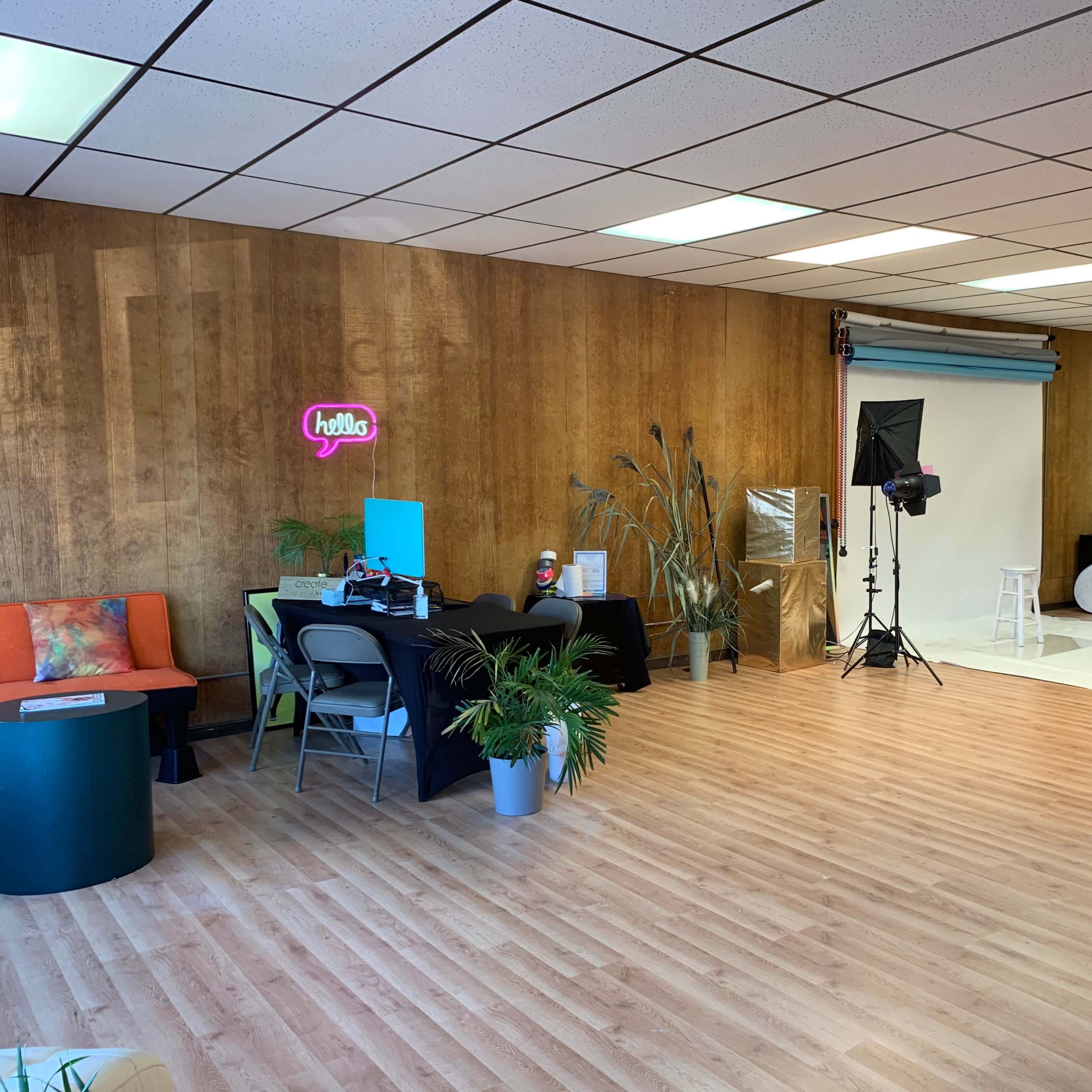 A spacious studio with wooden walls, a greeting sign, display furniture, and photography equipment set up for a shoot.