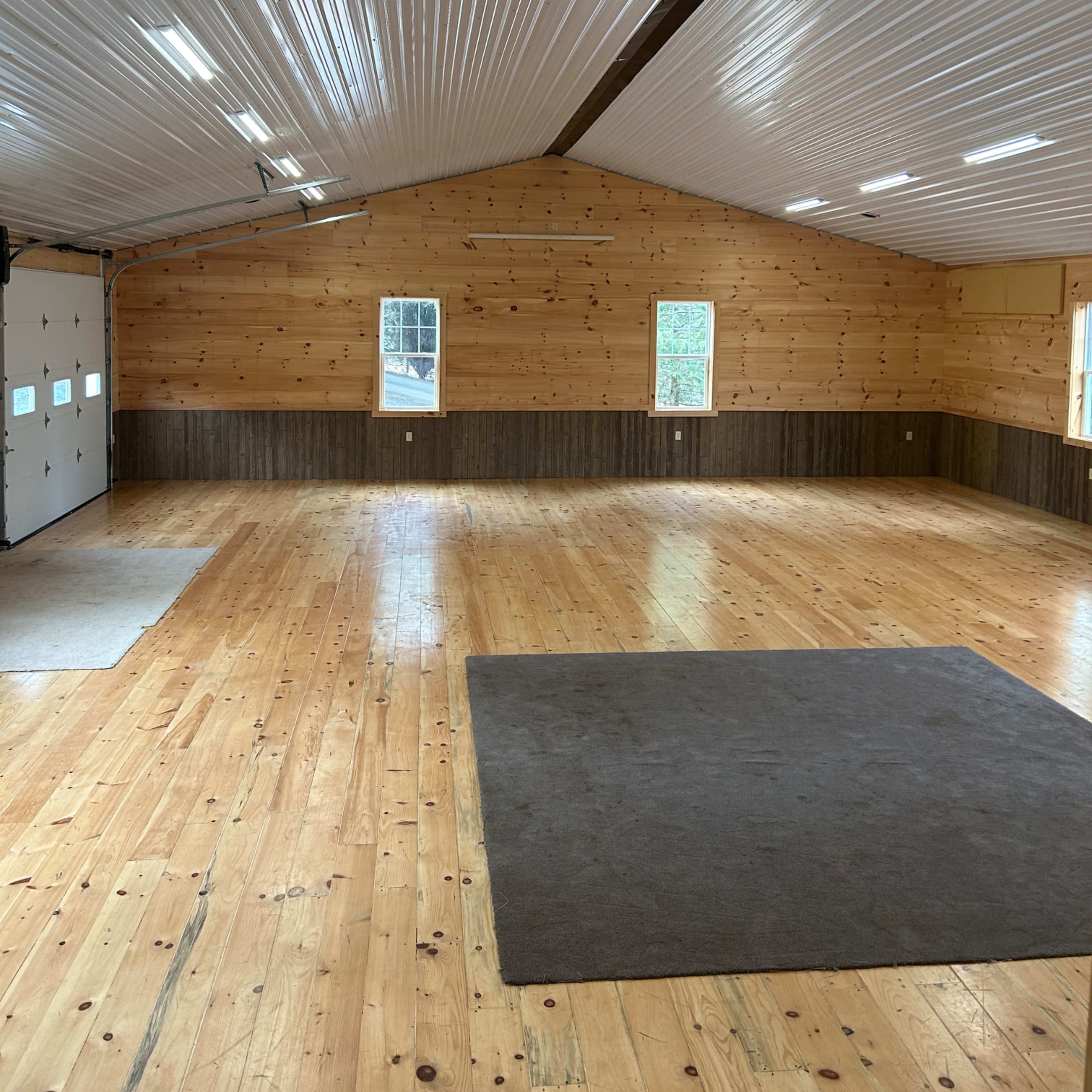 The interior of a spacious building features wooden walls, a high ceiling, and a polished wooden floor with minimal furnishings.