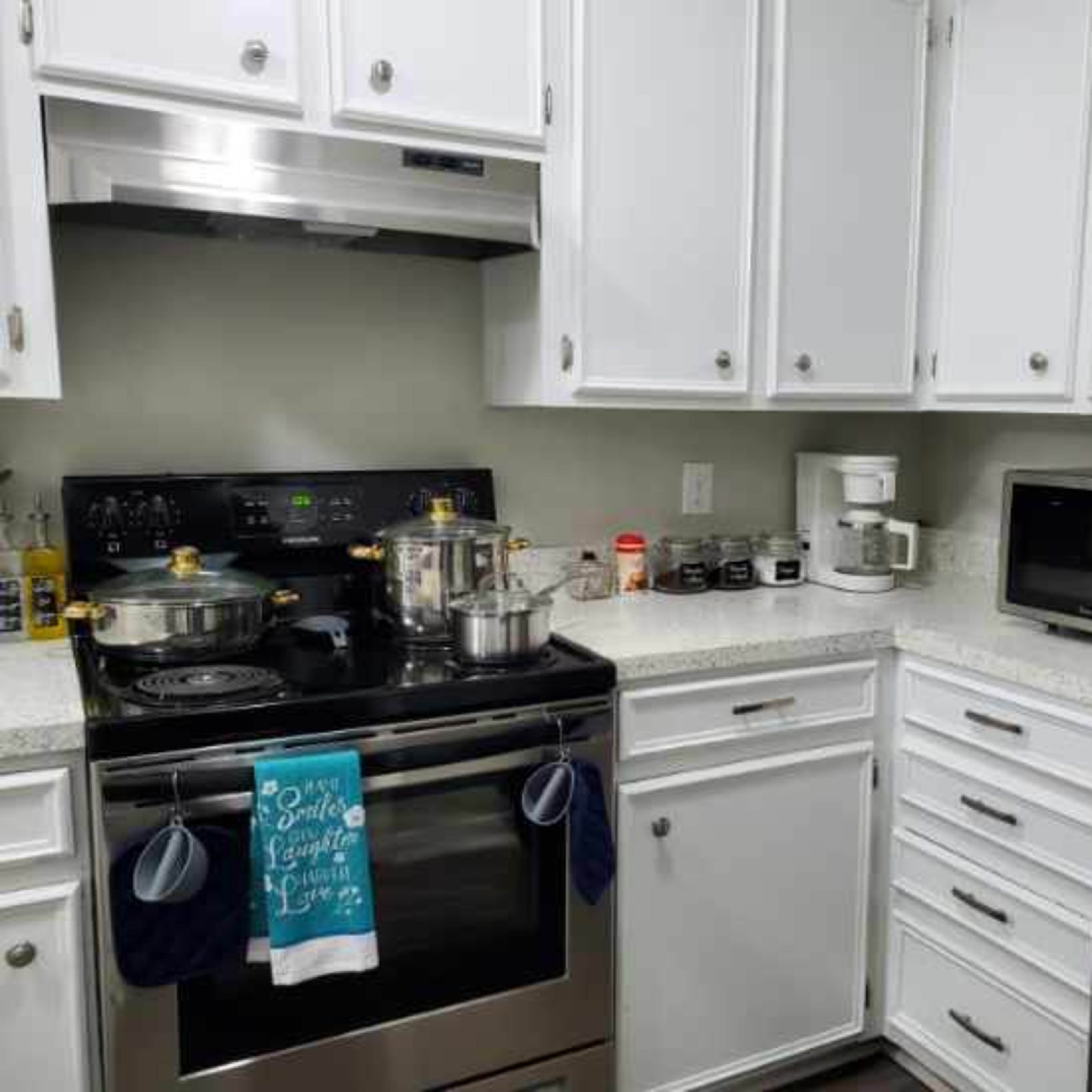 A modern kitchen features a stainless steel refrigerator, an oven with pots on the stove, and white cabinets filled with various kitchen supplies.