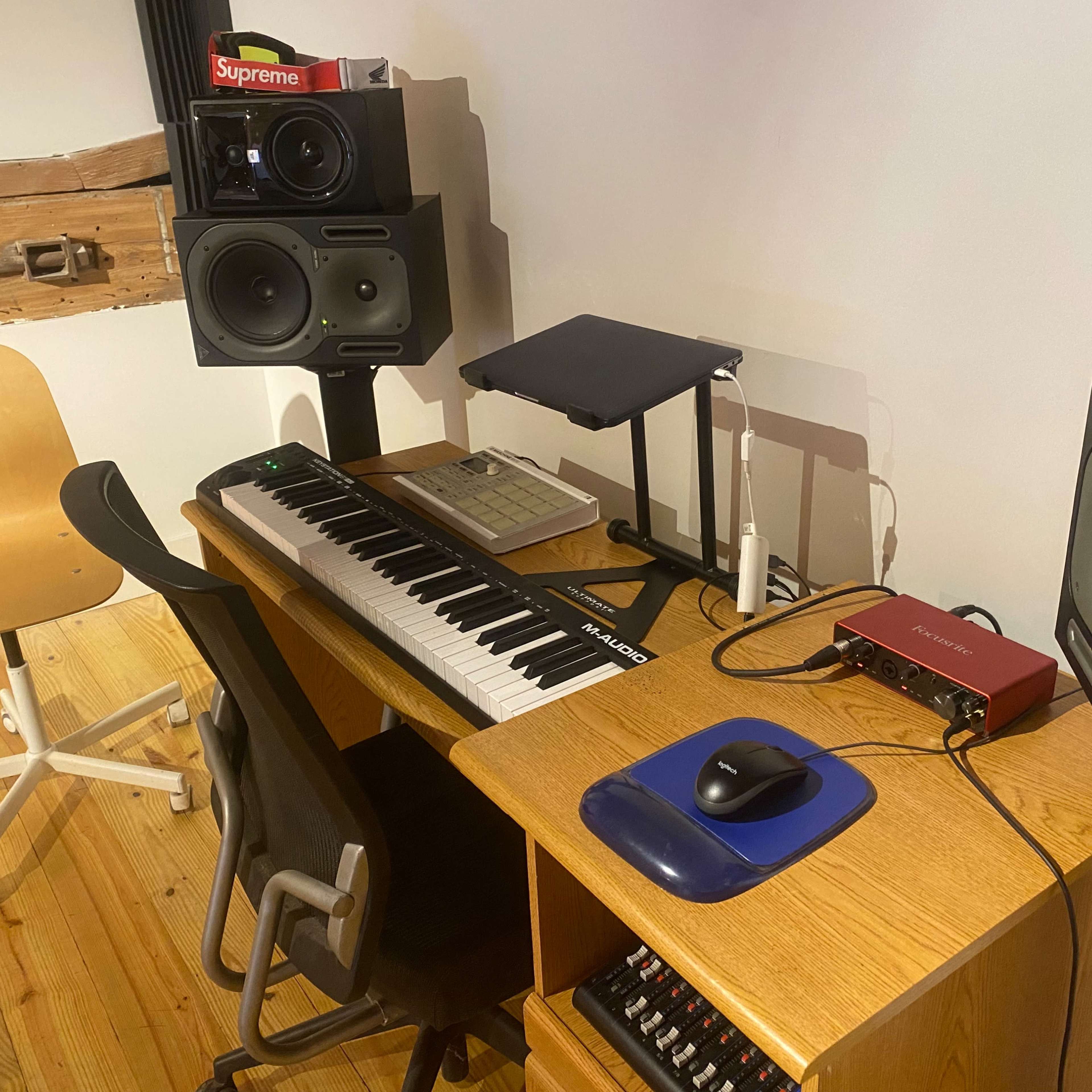 A wooden desk with a keyboard, audio interface, and two studio monitors set in a music production space.
