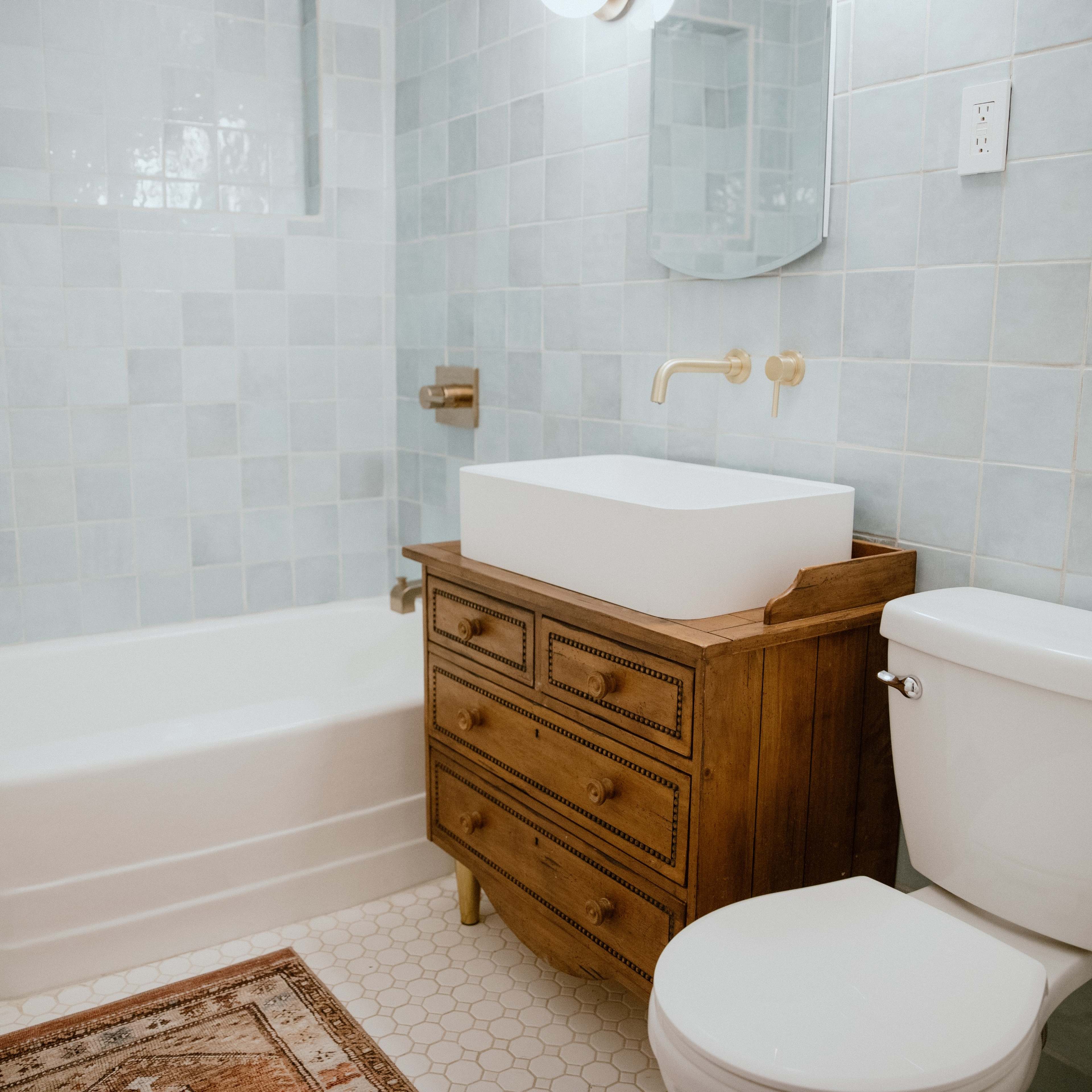 The bathroom features a freestanding tub, a wooden vanity with a square sink, a toilet, and blue tiled walls.
