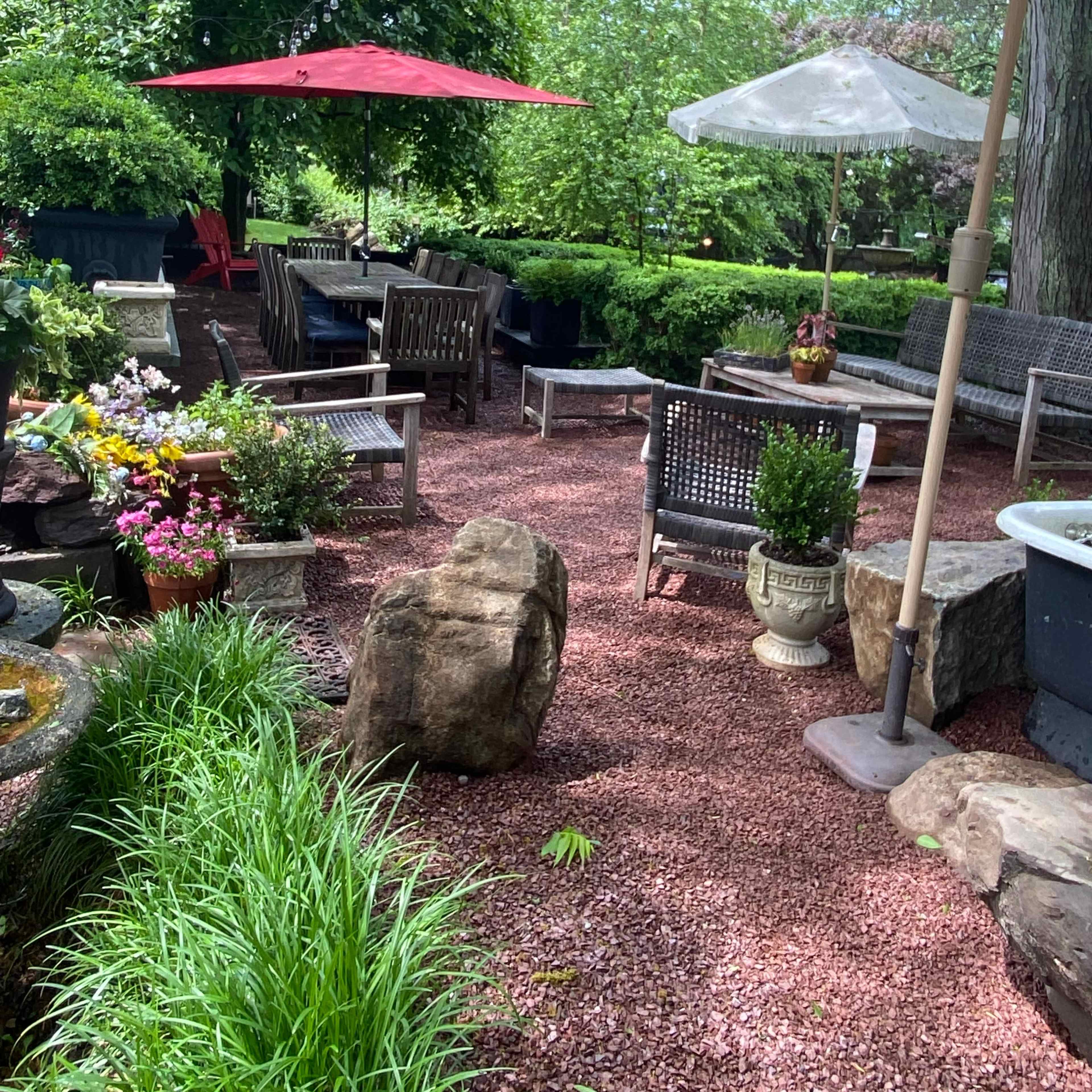 The scene features a landscaped garden area with stone pathways, seating arrangements under umbrellas, and decorative plants.