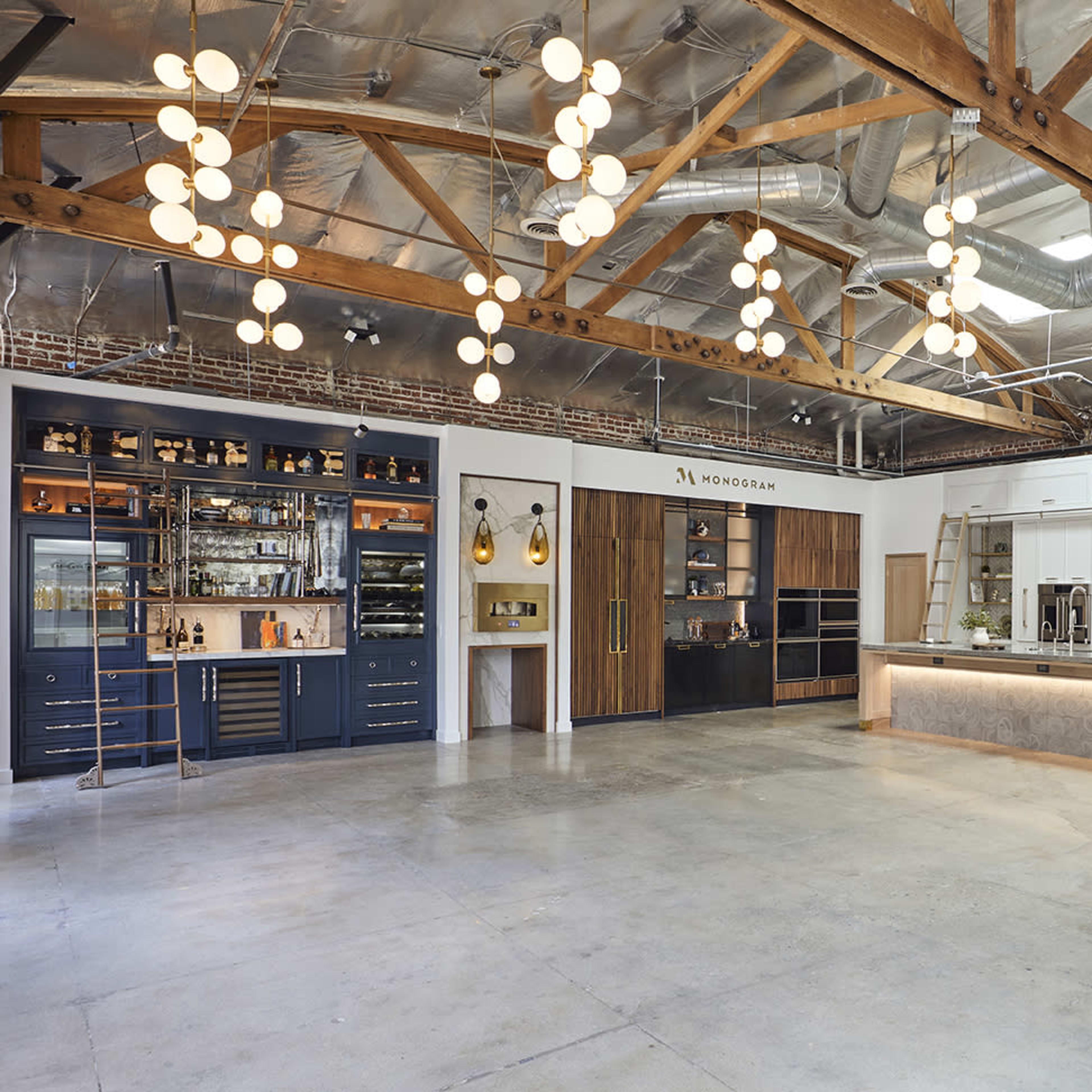 A modern kitchen showroom with wooden beams, pendant lighting, and various cabinetry styles displayed along the walls.