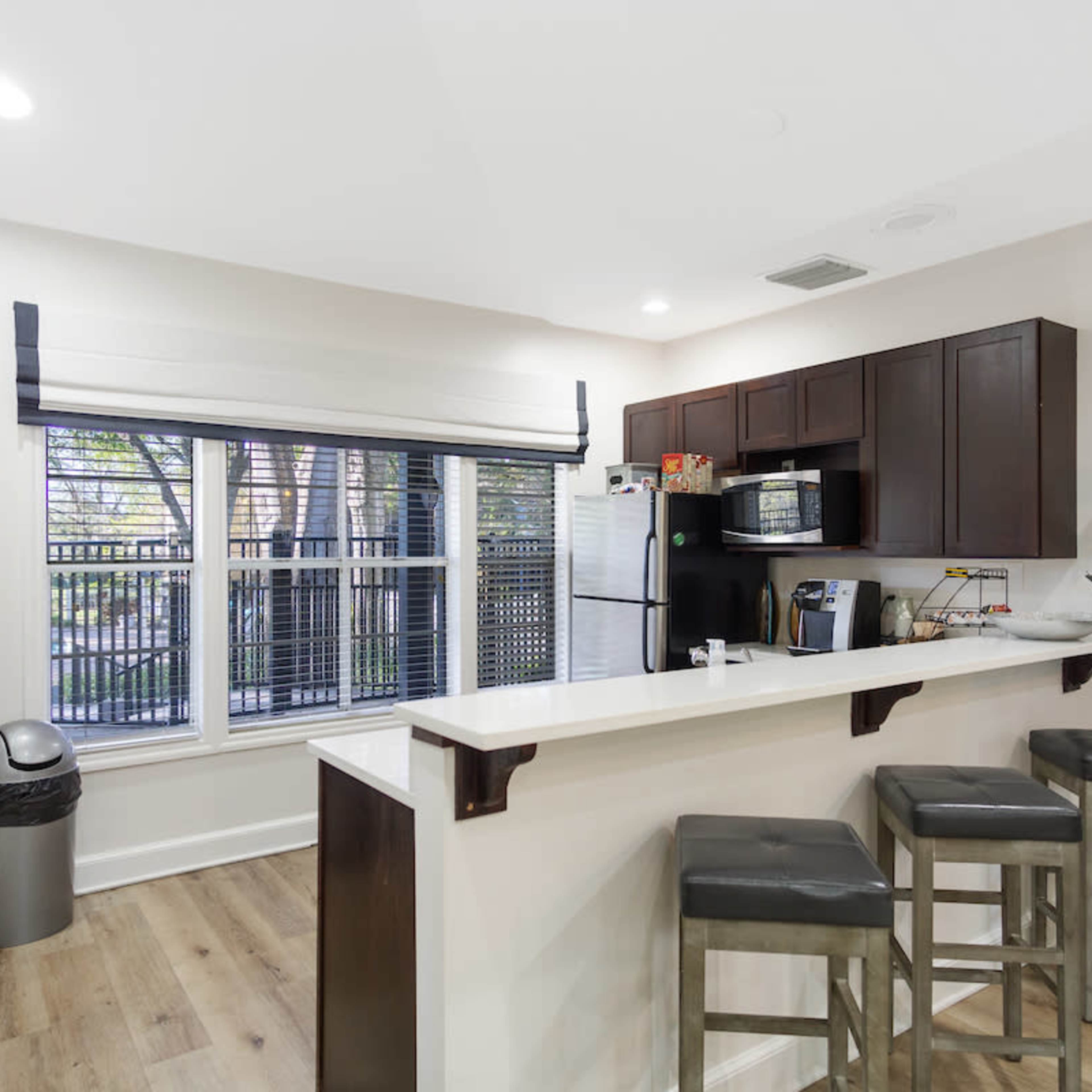 A modern kitchen features dark cabinetry, a breakfast bar with stools, and large windows overlooking a courtyard.