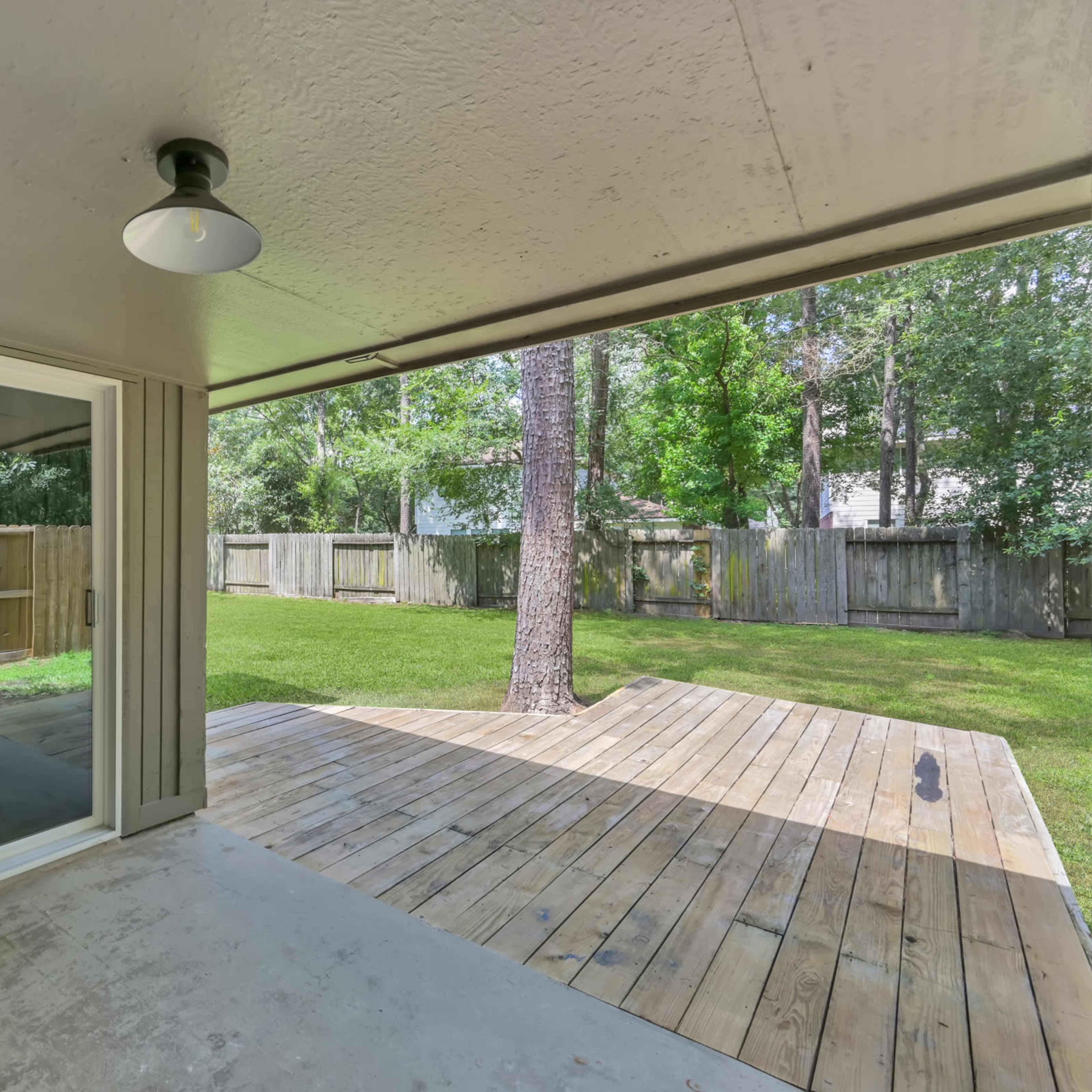 A covered patio area with a sliding glass door overlooking a grassy backyard and a wooden deck.
