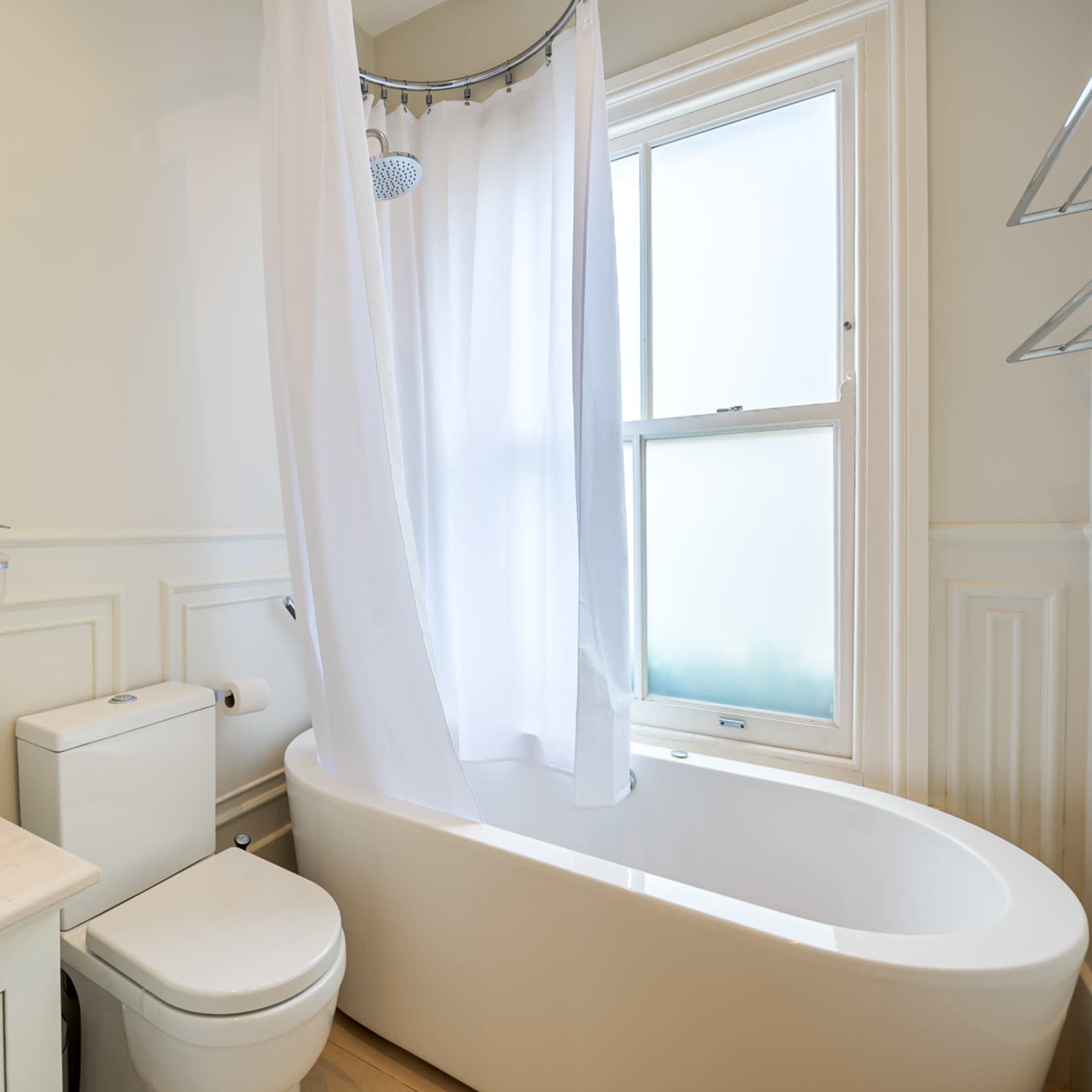 A bathroom featuring a bathtub with a shower curtain, a toilet, a sink with a round basin, and a large window allowing natural light.