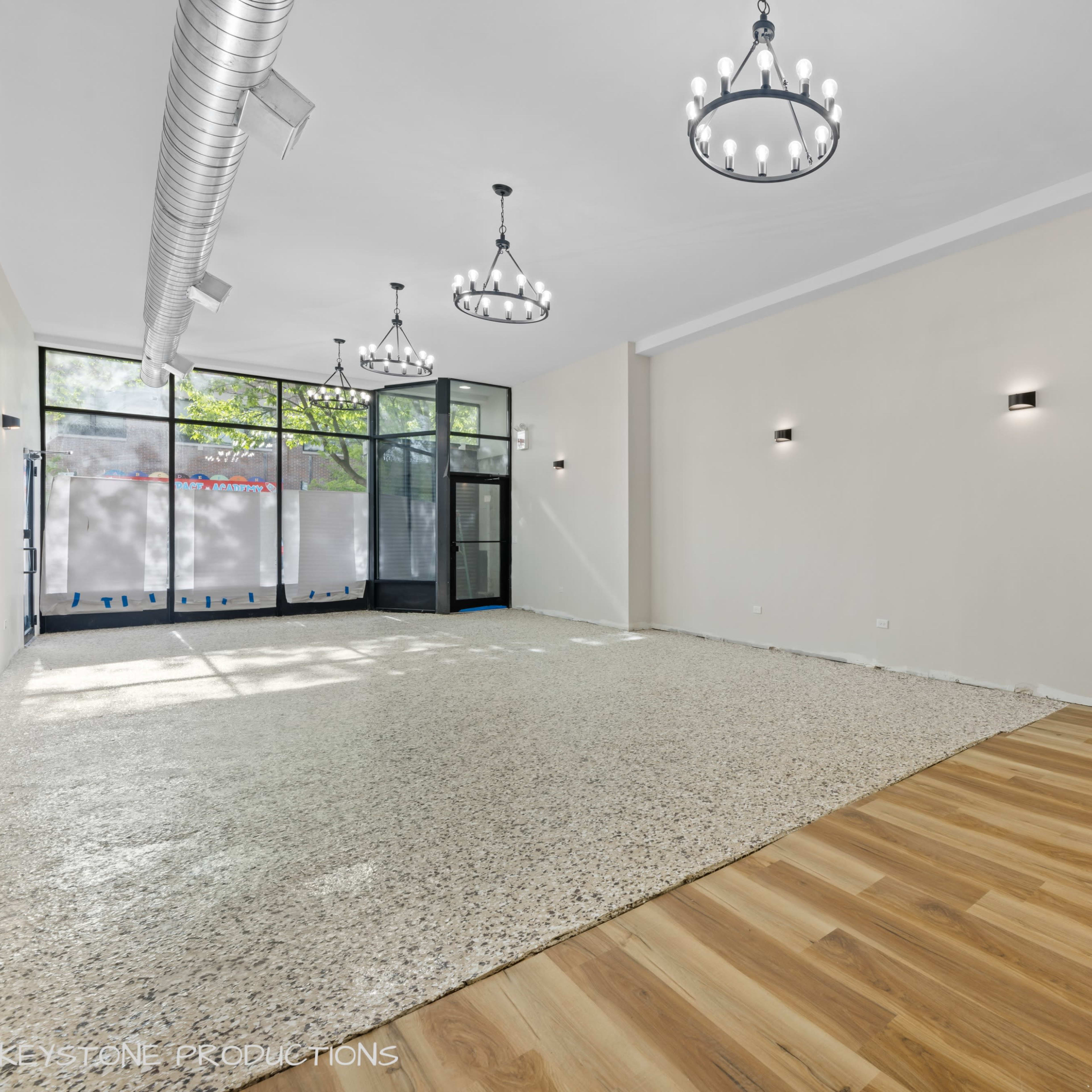 A spacious commercial room with a mix of polished concrete and wooden flooring, illuminated by several chandeliers and wall sconces.