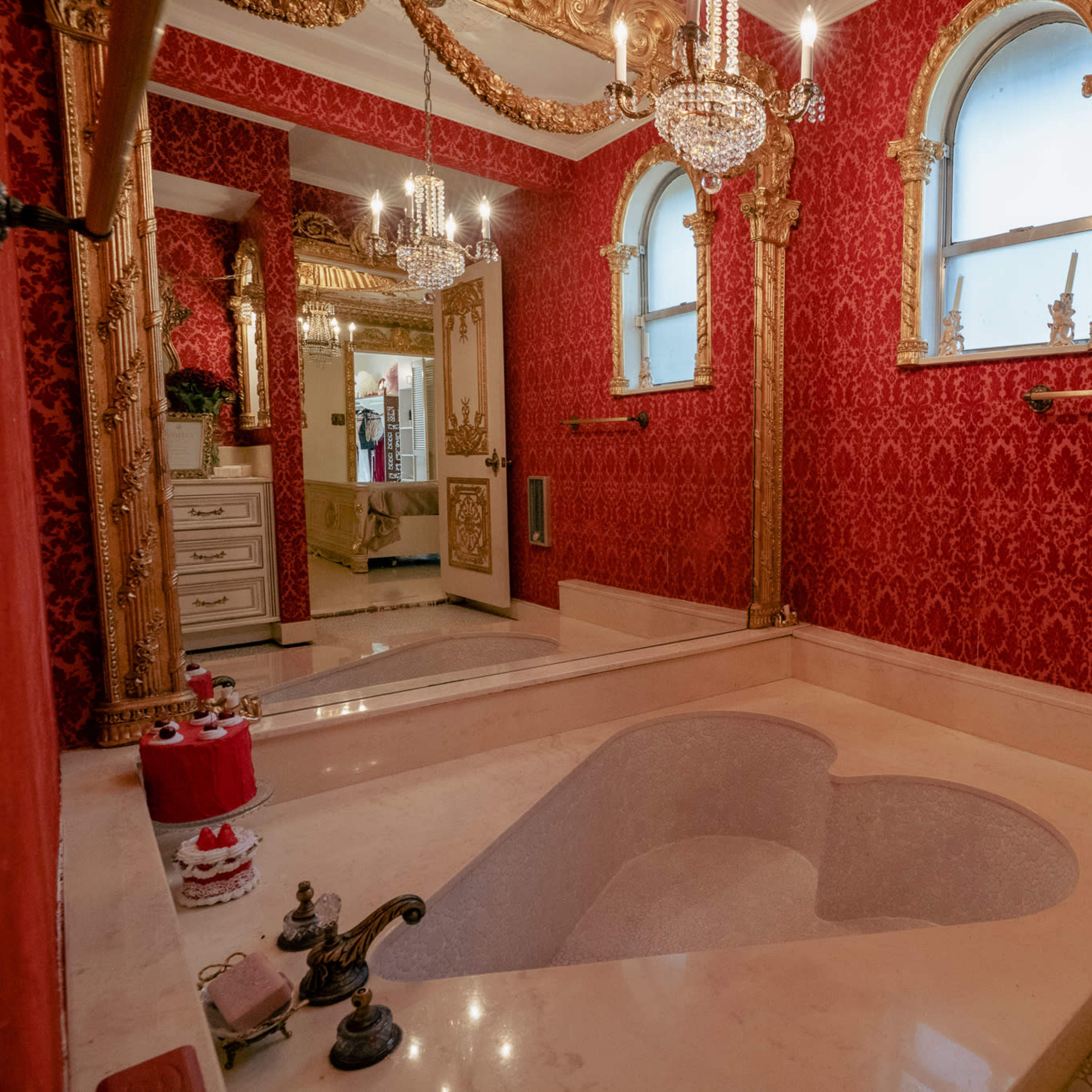 The bathroom features a heart-shaped bathtub surrounded by red patterned wallpaper and ornate golden accents.