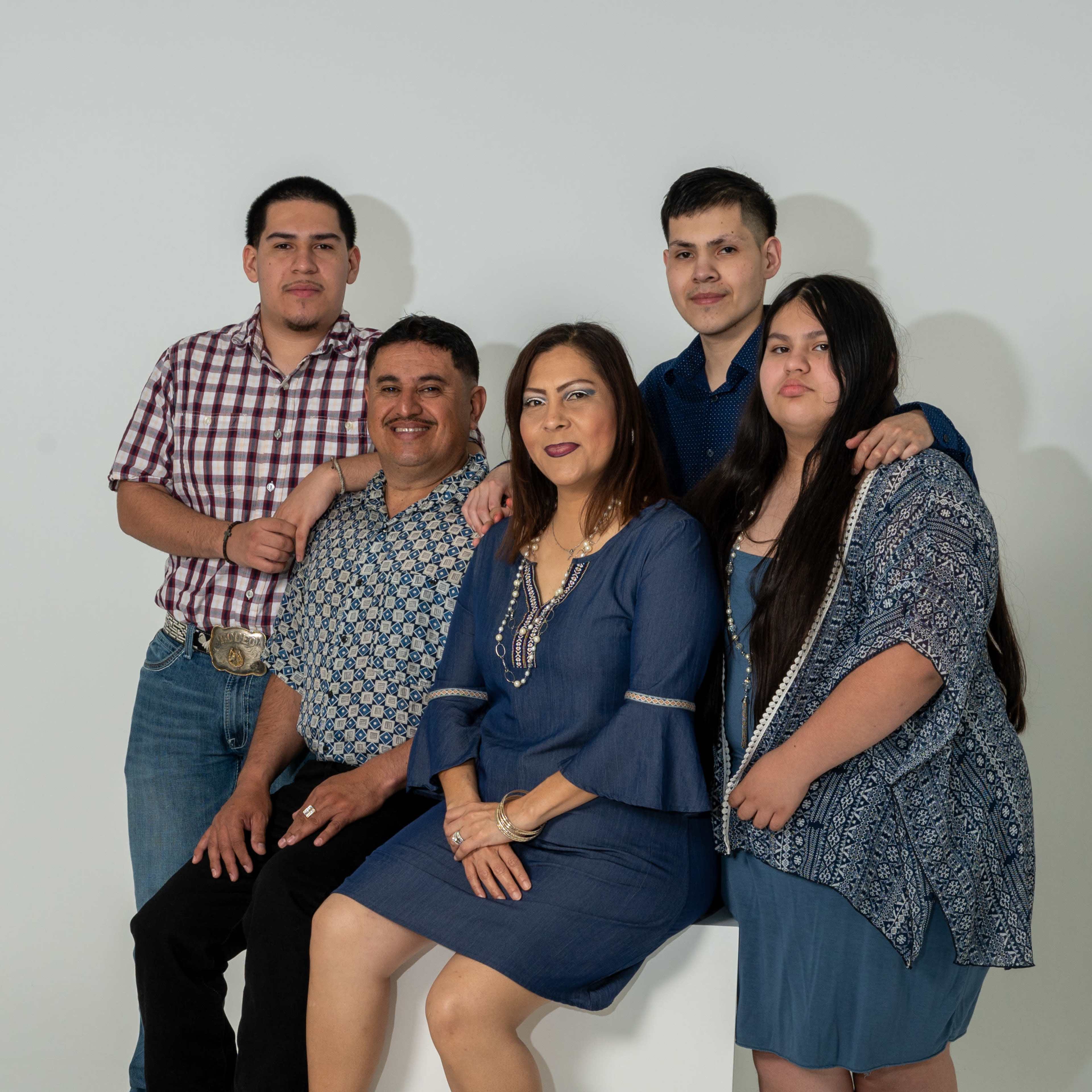 A family poses together with a neutral background, featuring three adults and two teenagers arranged around a white pedestal.