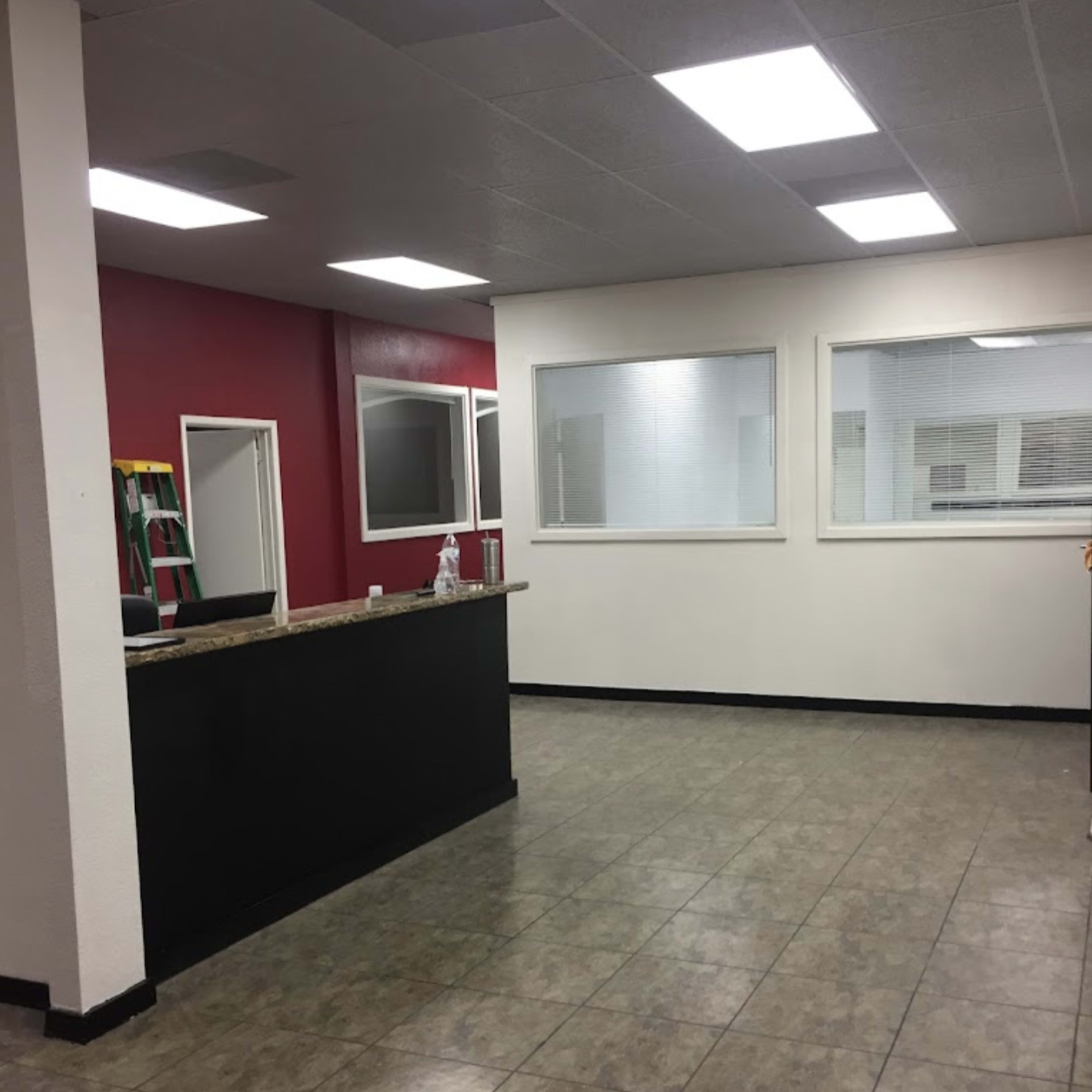 An office interior with a reception desk, a red accent wall, and large windows letting in natural light.