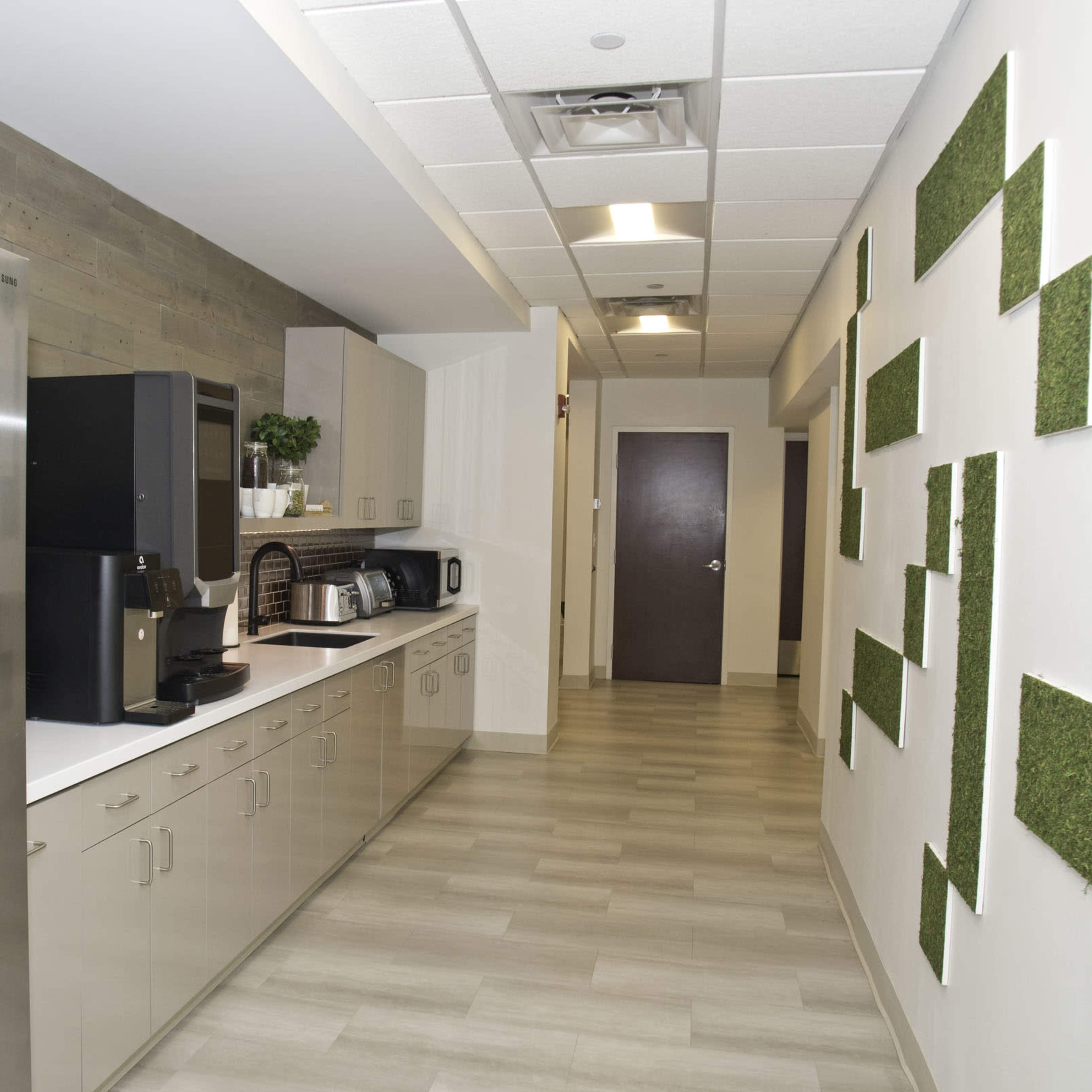 A modern kitchen area featuring stainless steel appliances, cabinetry, and a wall adorned with green moss panels.