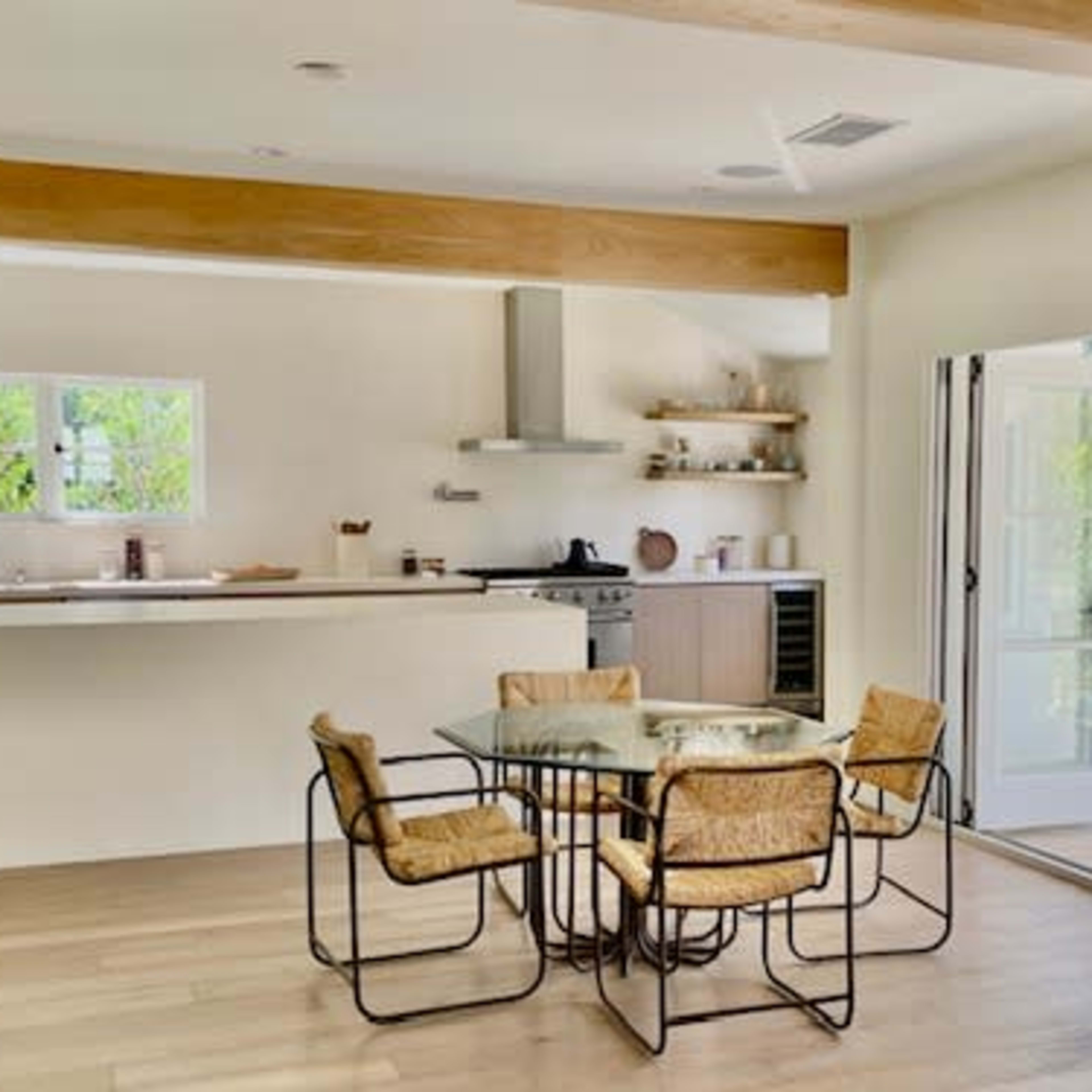 A spacious kitchen and dining area features a glass-top table surrounded by four chairs, with a doorway leading to an outdoor space.