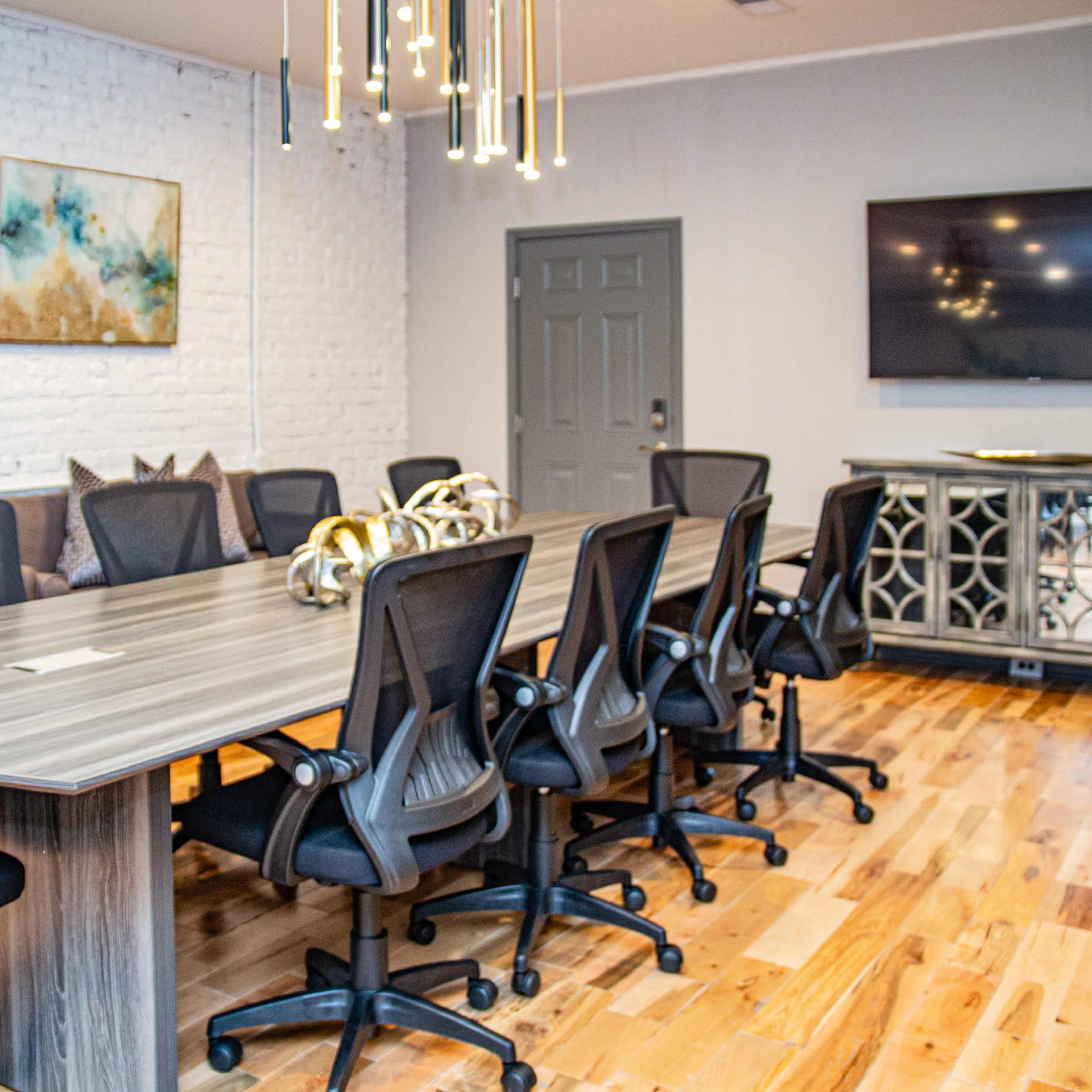 A modern conference room with a long table surrounded by eight black office chairs, a television on the wall, and decorative elements on the side.