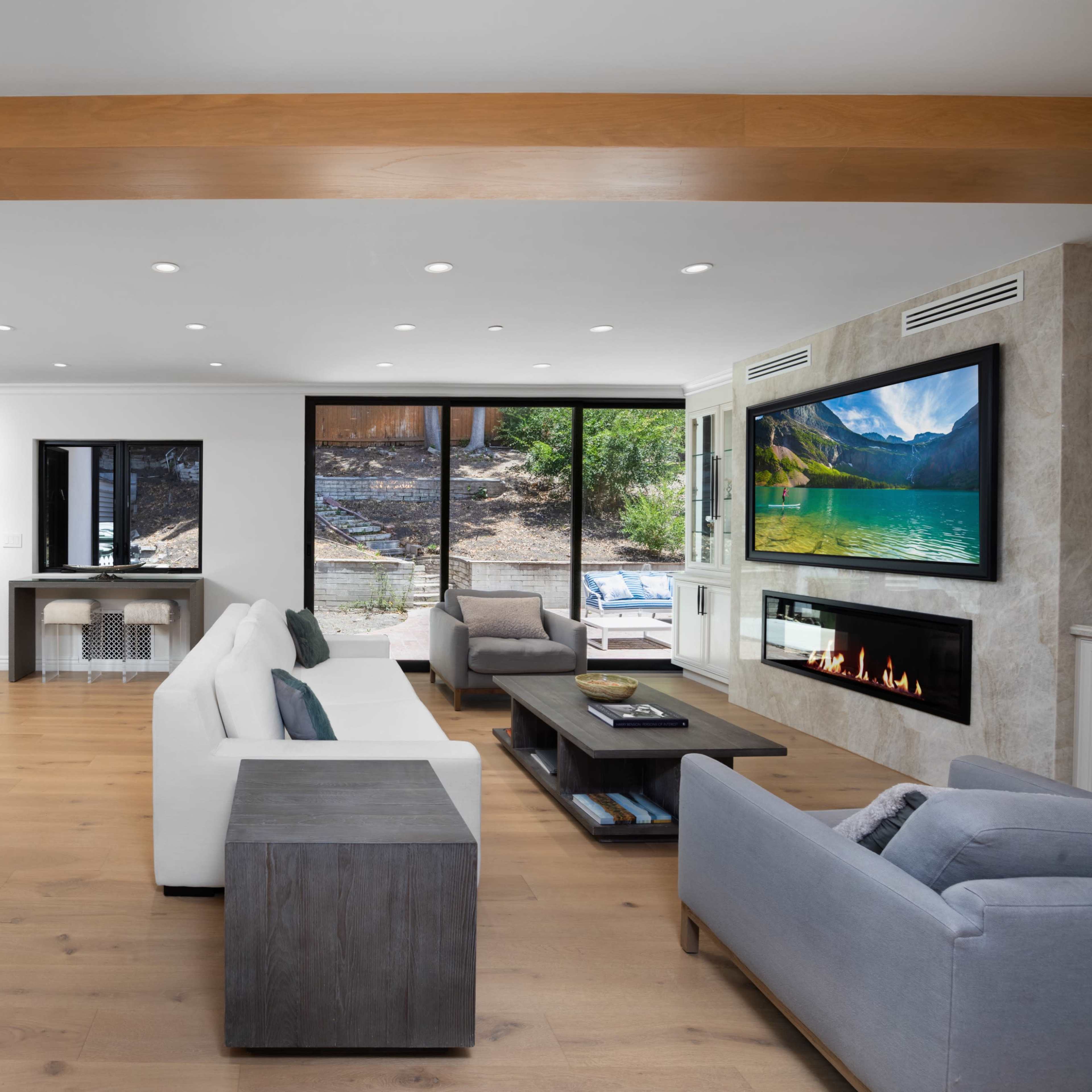 The open living space features a modern kitchen area, a comfortable seating arrangement, a fireplace, and large windows overlooking an outdoor patio.