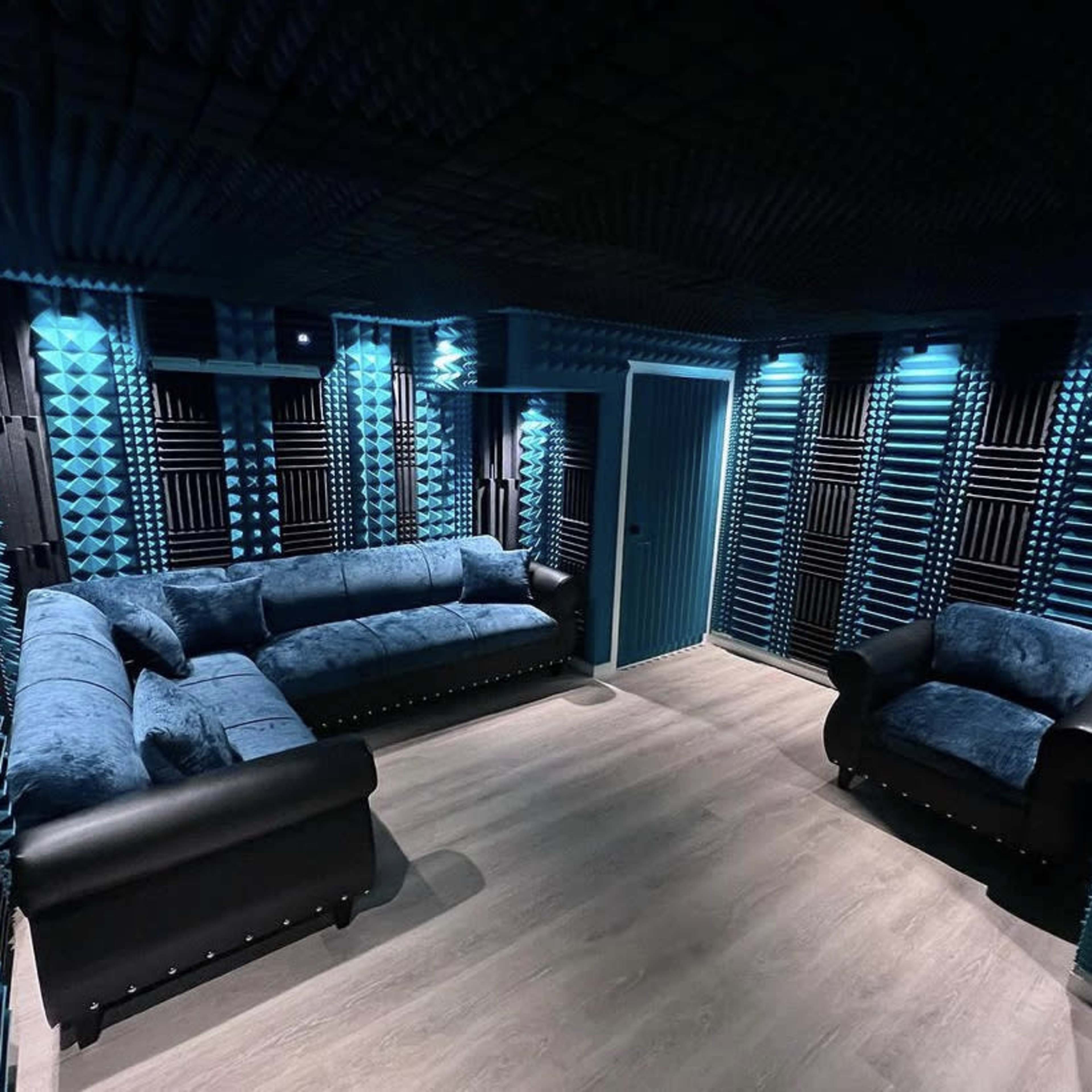 A soundproof room featuring blue acoustic foam panels on the walls, a gray sofa, and a black armchair.