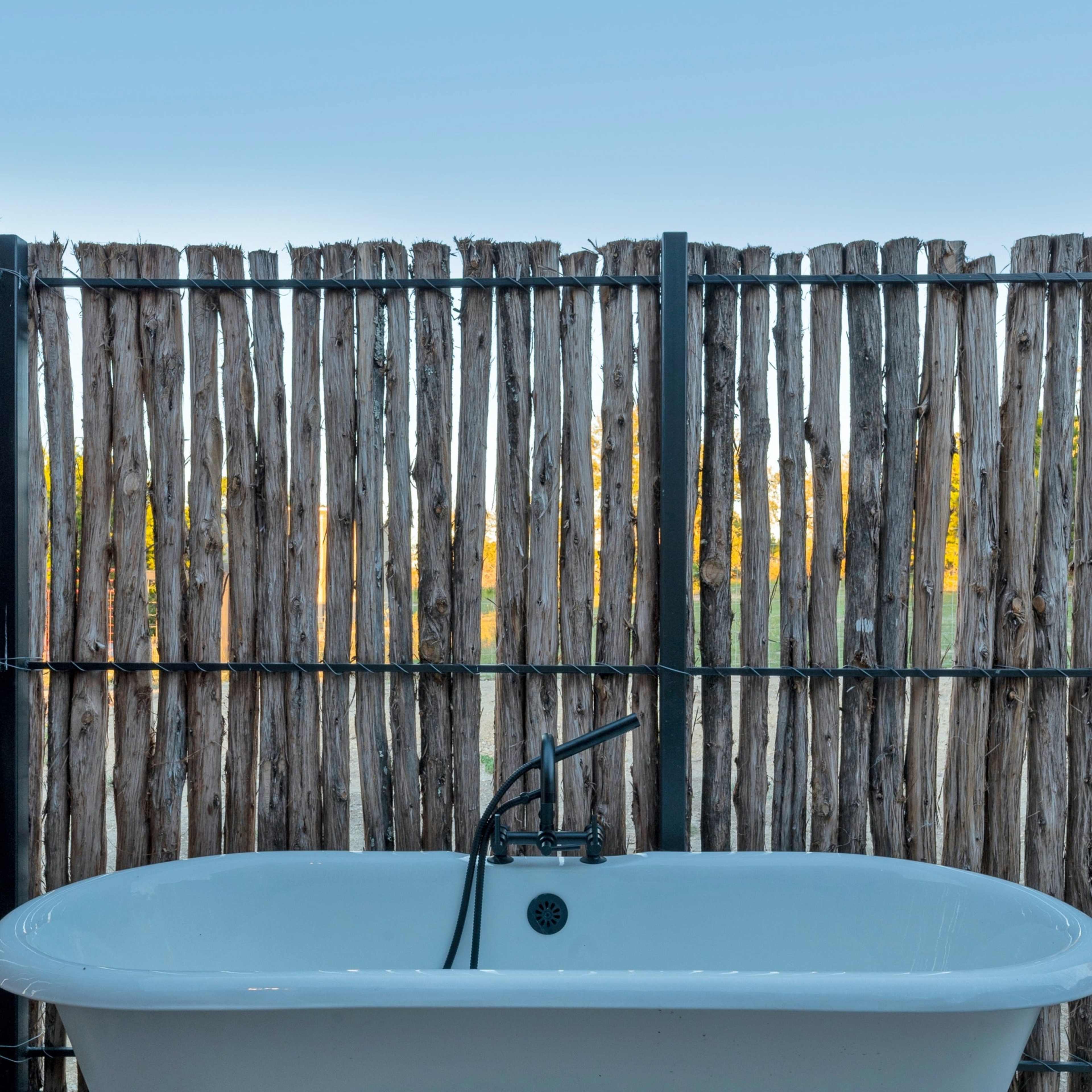 A white freestanding bathtub is positioned in front of a wooden fence.