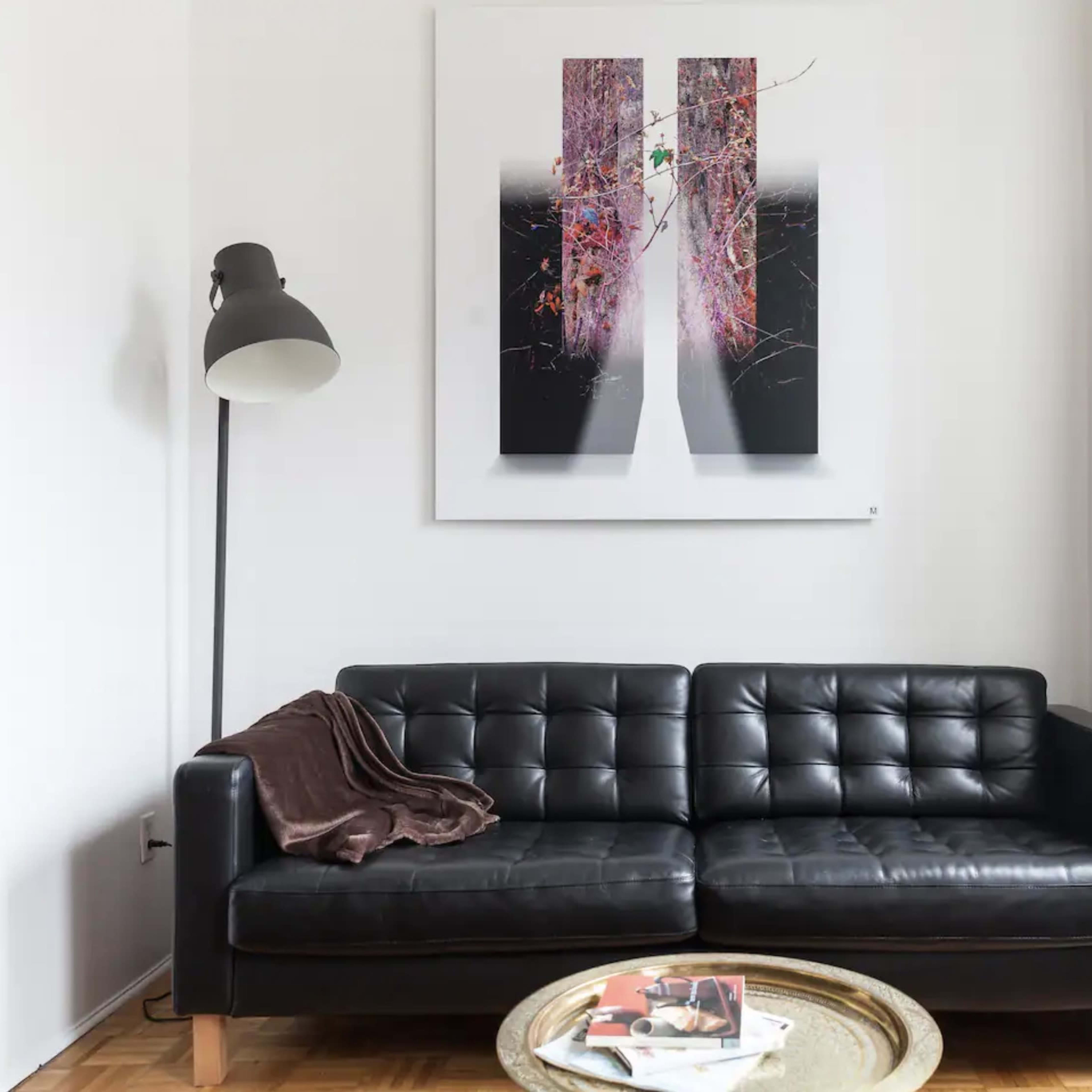 A black leather sofa sits against a white wall, accompanied by a large abstract artwork and a small coffee table with magazines.