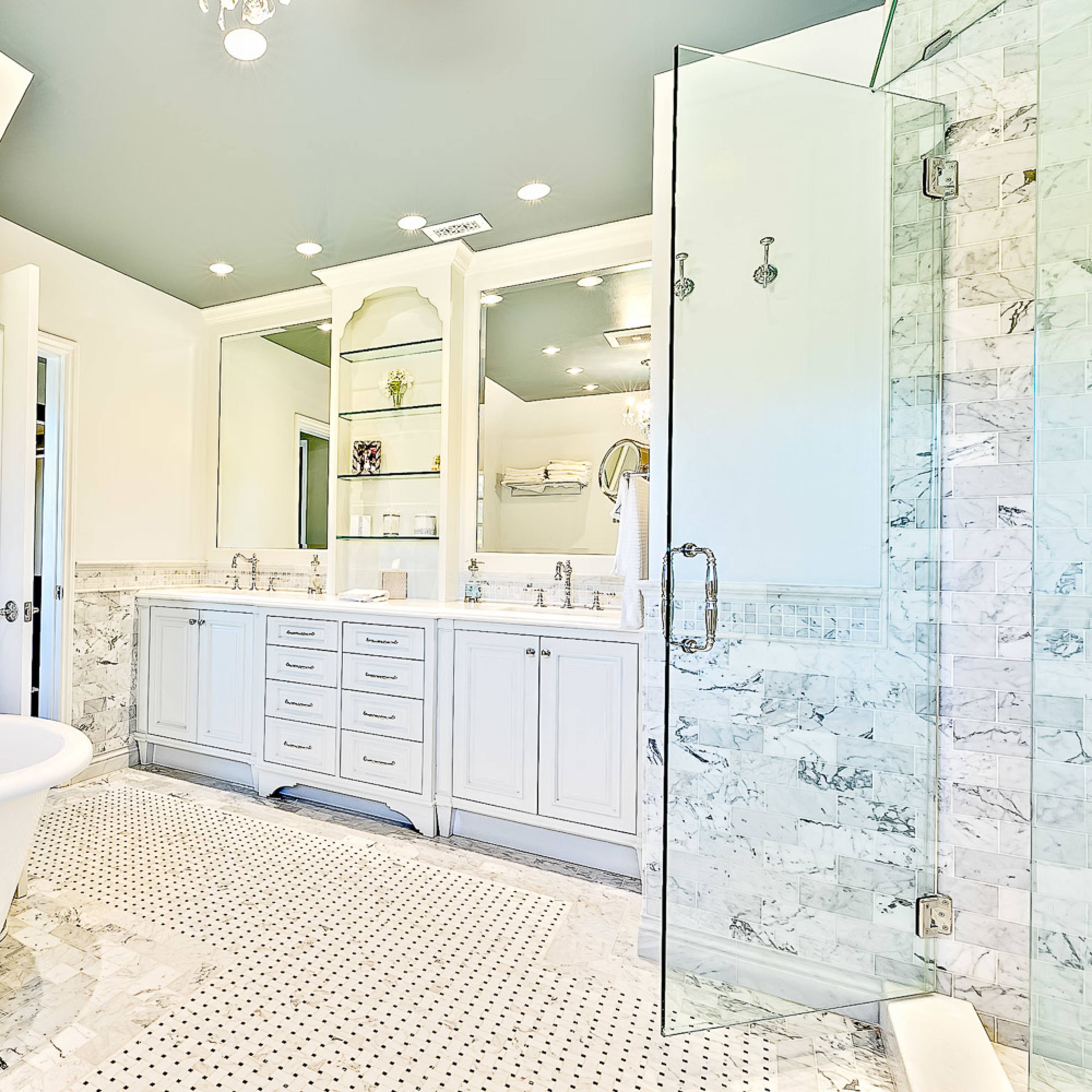 A spacious bathroom with a freestanding tub, a glass shower enclosure, double sinks, and marble flooring and walls.