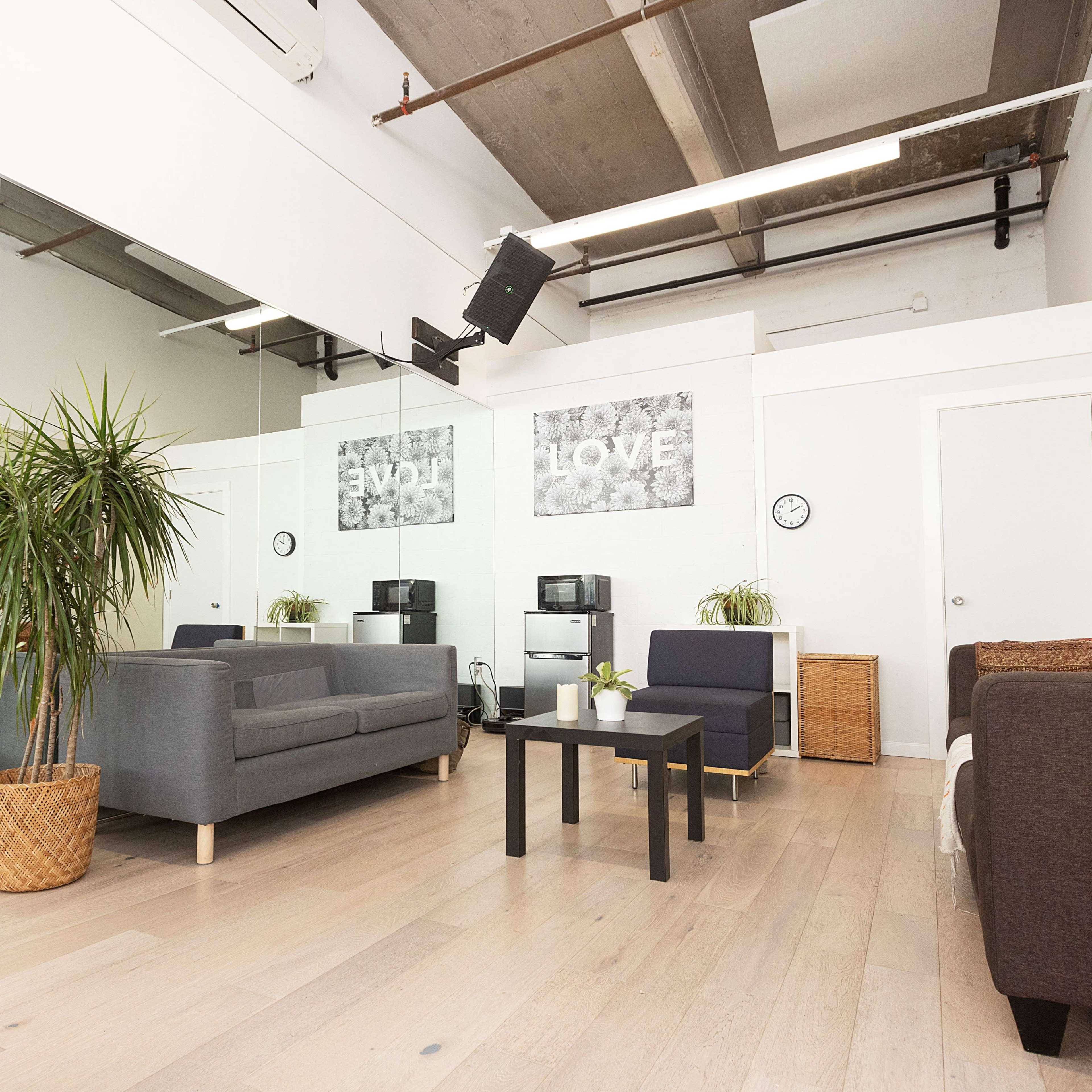 A spacious room with light wooden flooring, featuring several seating areas, plants, and wall art with the words "LOVE."