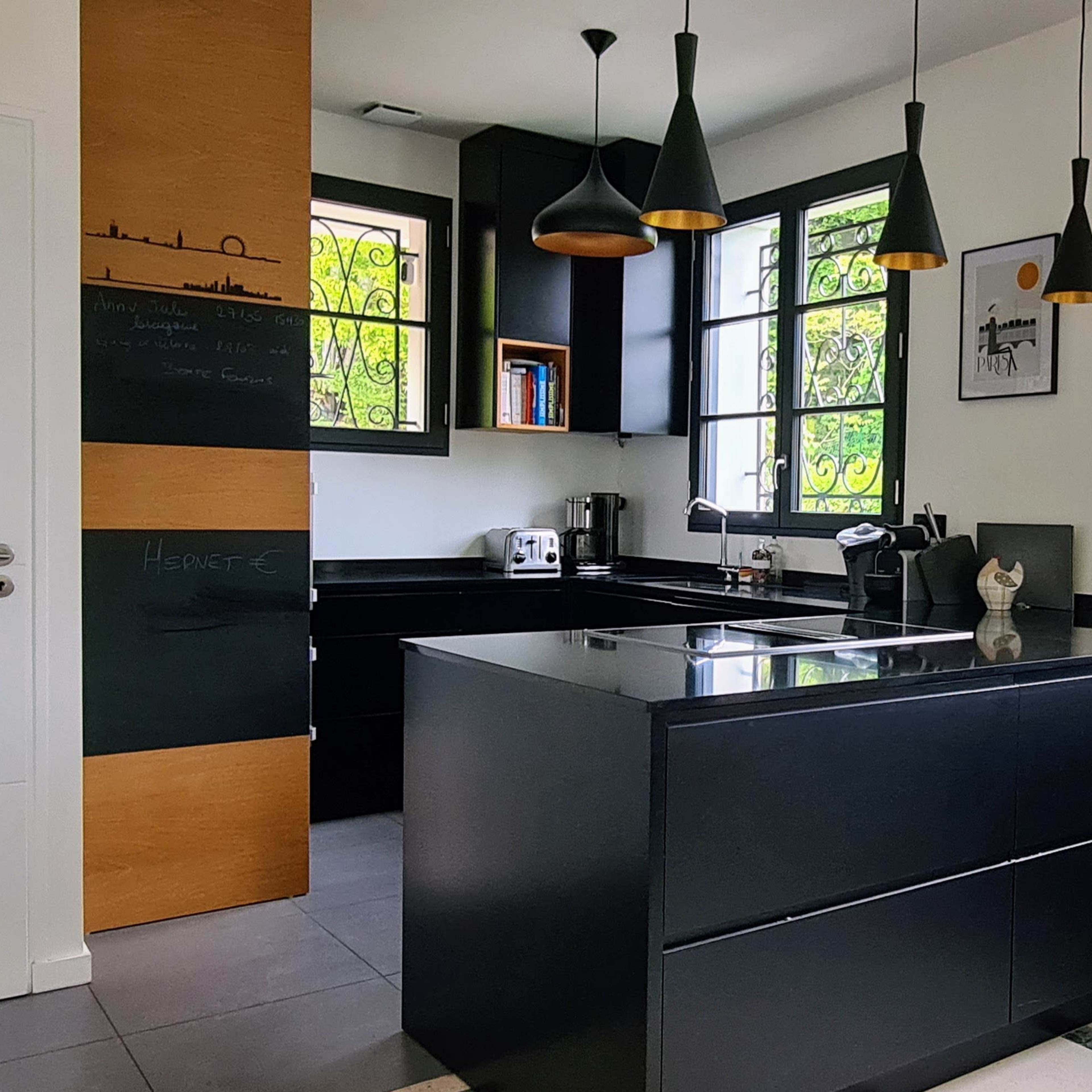 A modern kitchen with black cabinetry, a large island, and natural light streaming through windows framed in black.