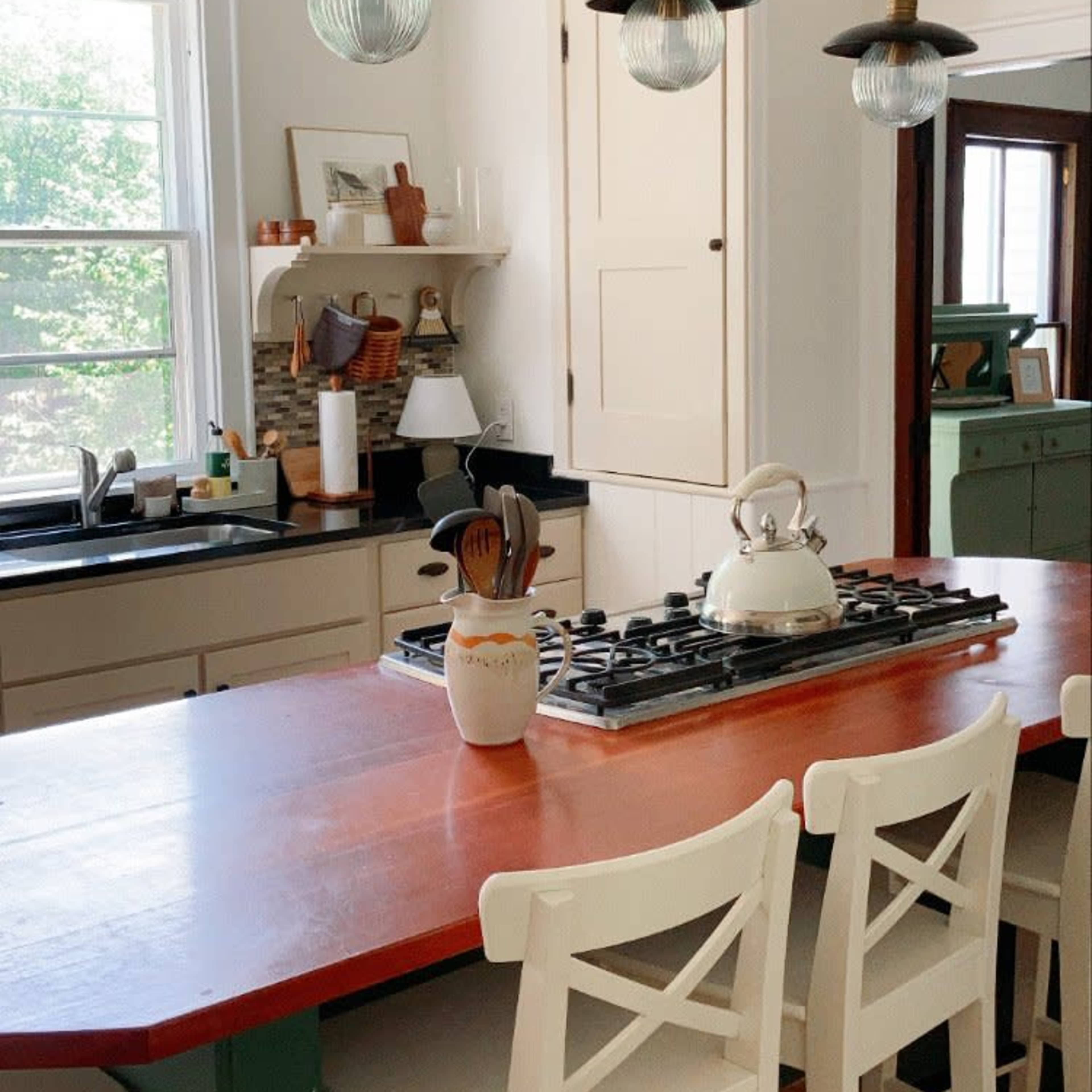 A bright kitchen featuring a wooden island with bar stools, a gas stove, and pendant lights hanging above.