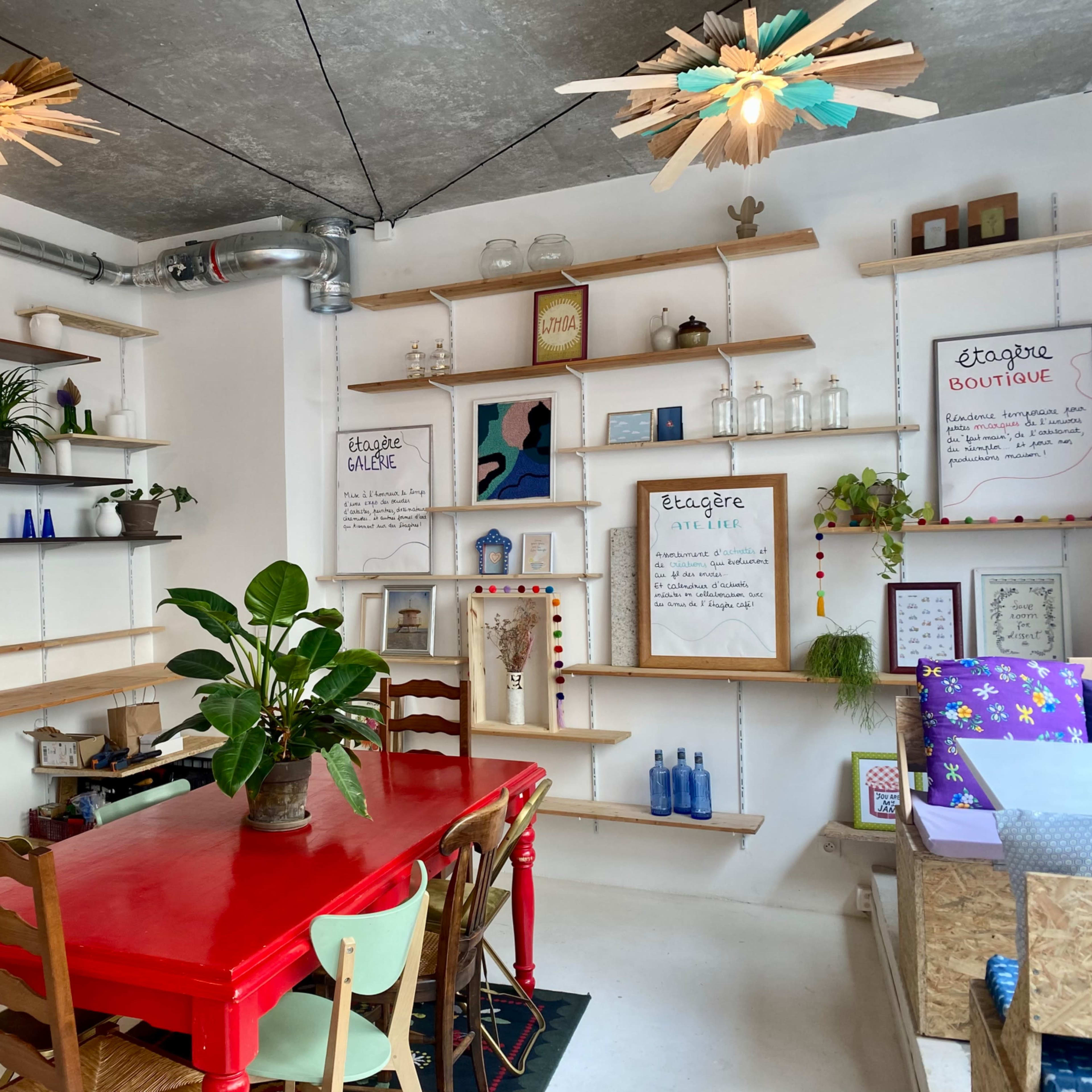 A bright, modern interior of a boutique featuring a red table with wooden chairs, shelves displaying various items, and unique ceiling fixtures.