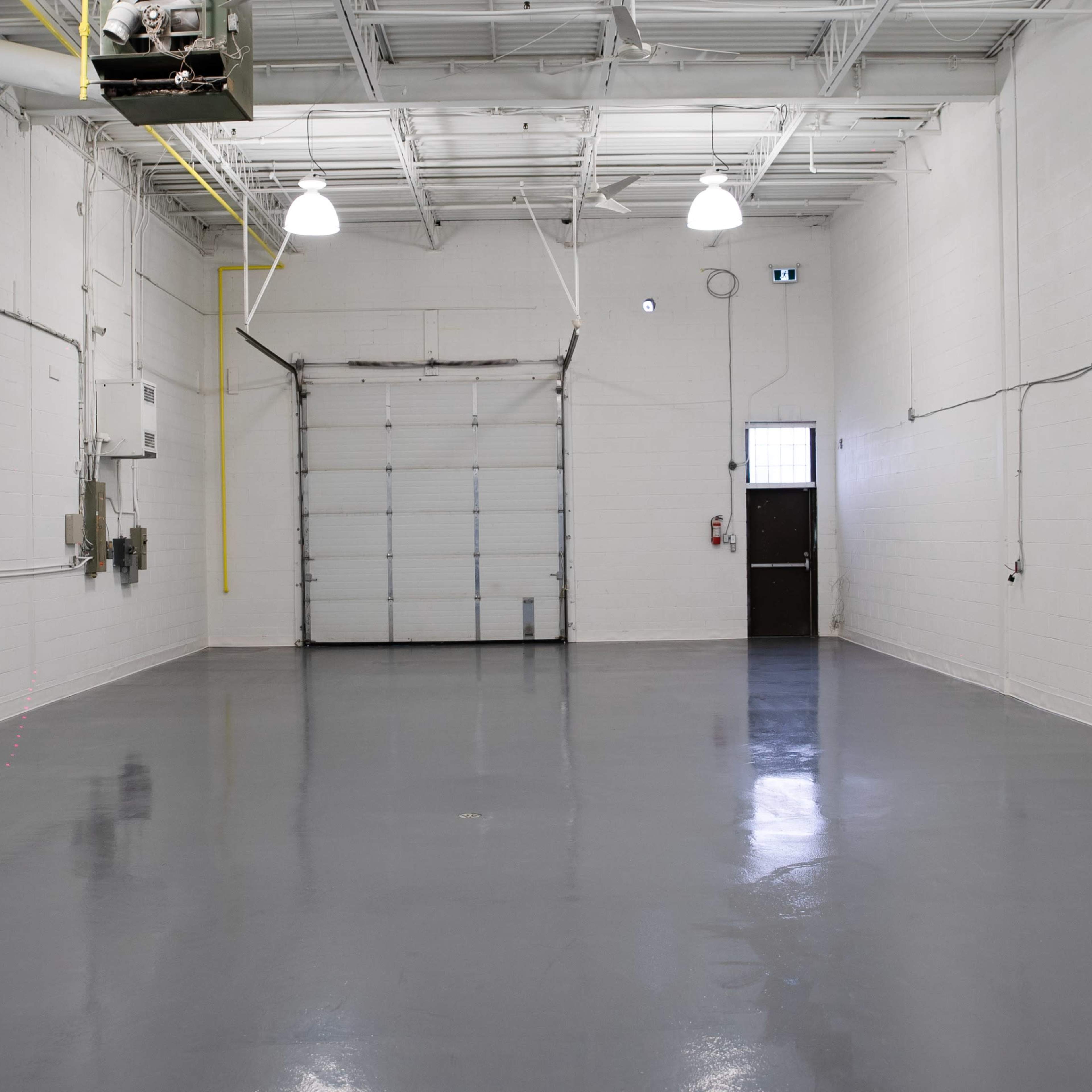 A spacious, empty warehouse with a concrete floor, white walls, and a large door at one end.