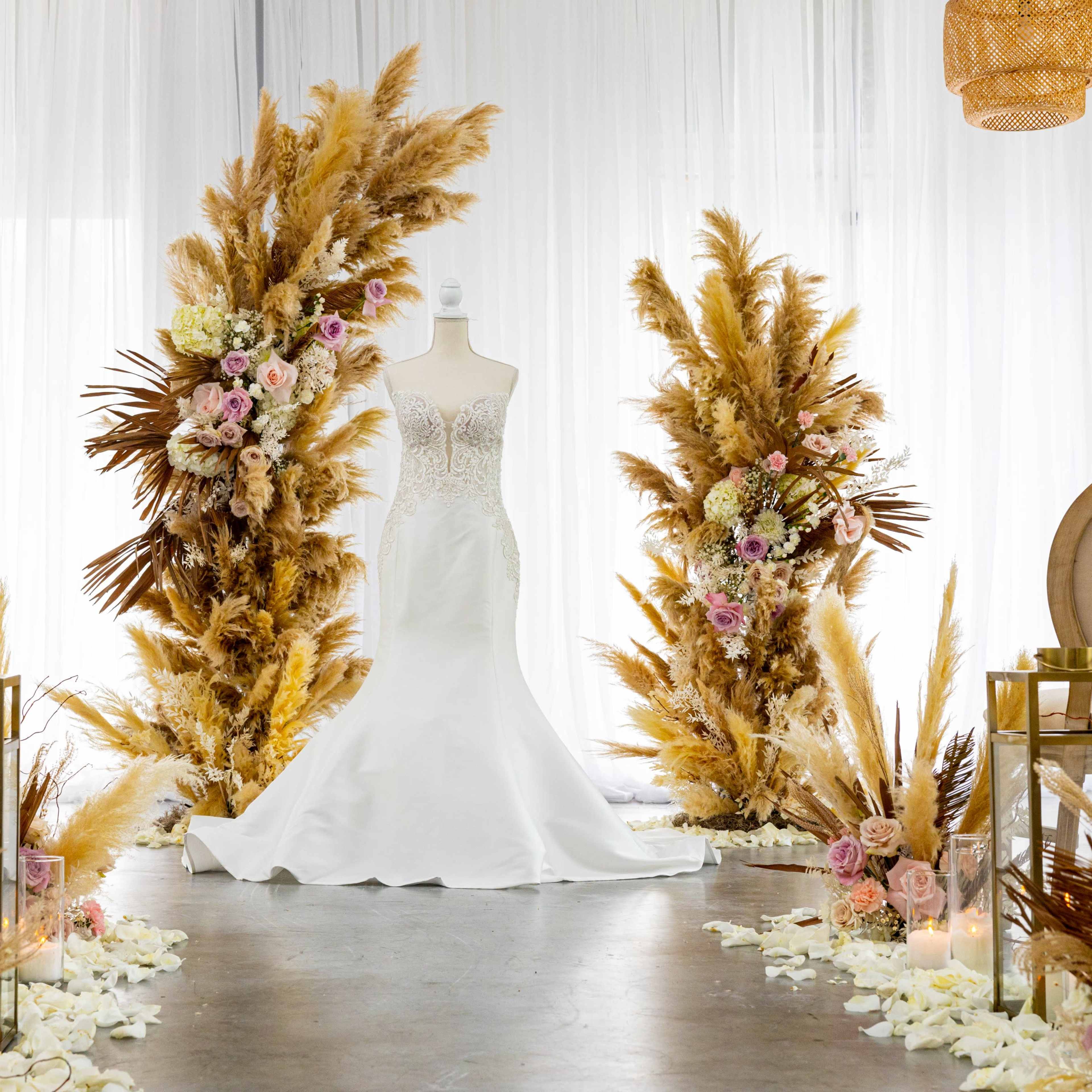 A wedding setup with a white bridal gown displayed on a mannequin, surrounded by floral arrangements and decorative elements made of pampas grass.