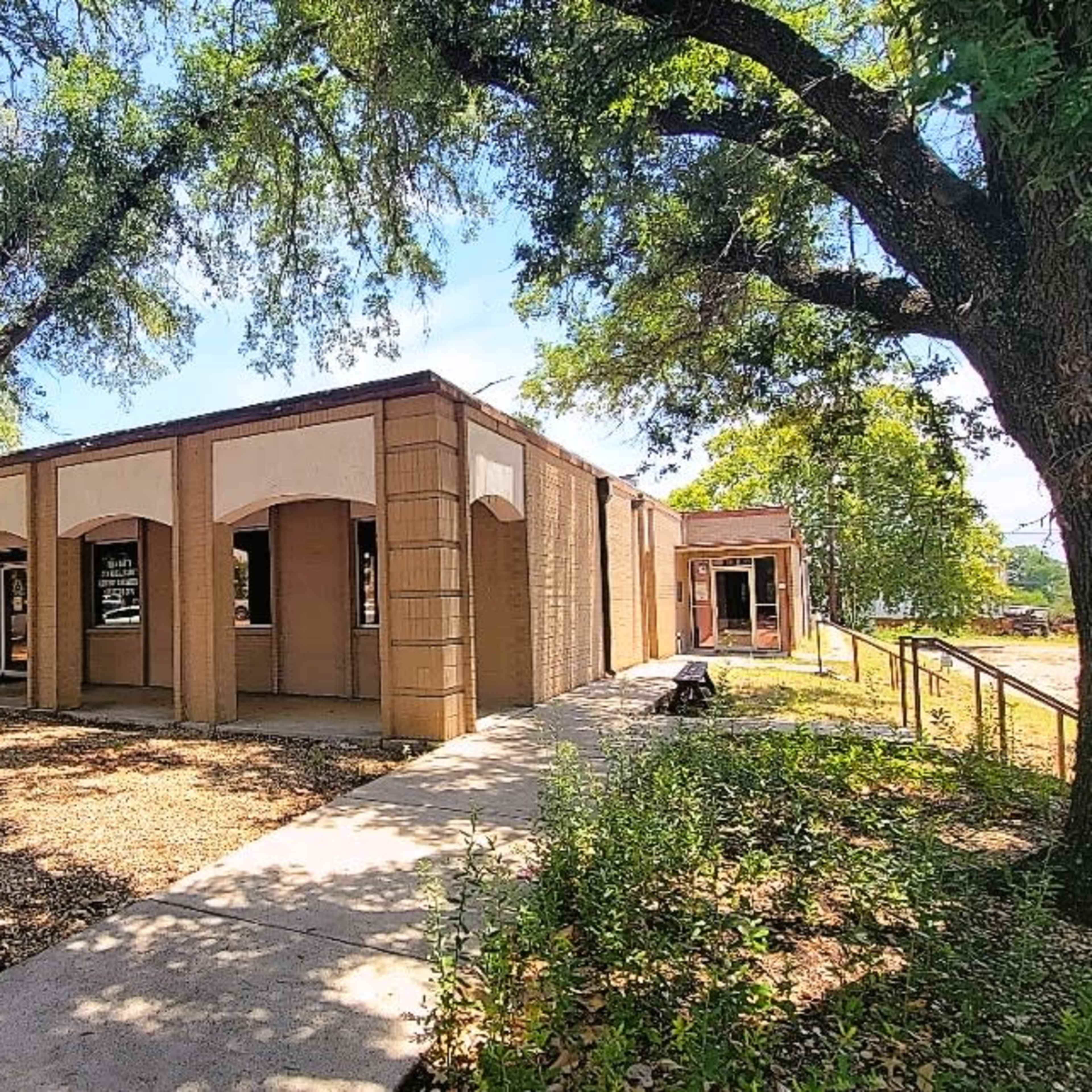A single-story building with arched entrances surrounded by trees and a sidewalk.