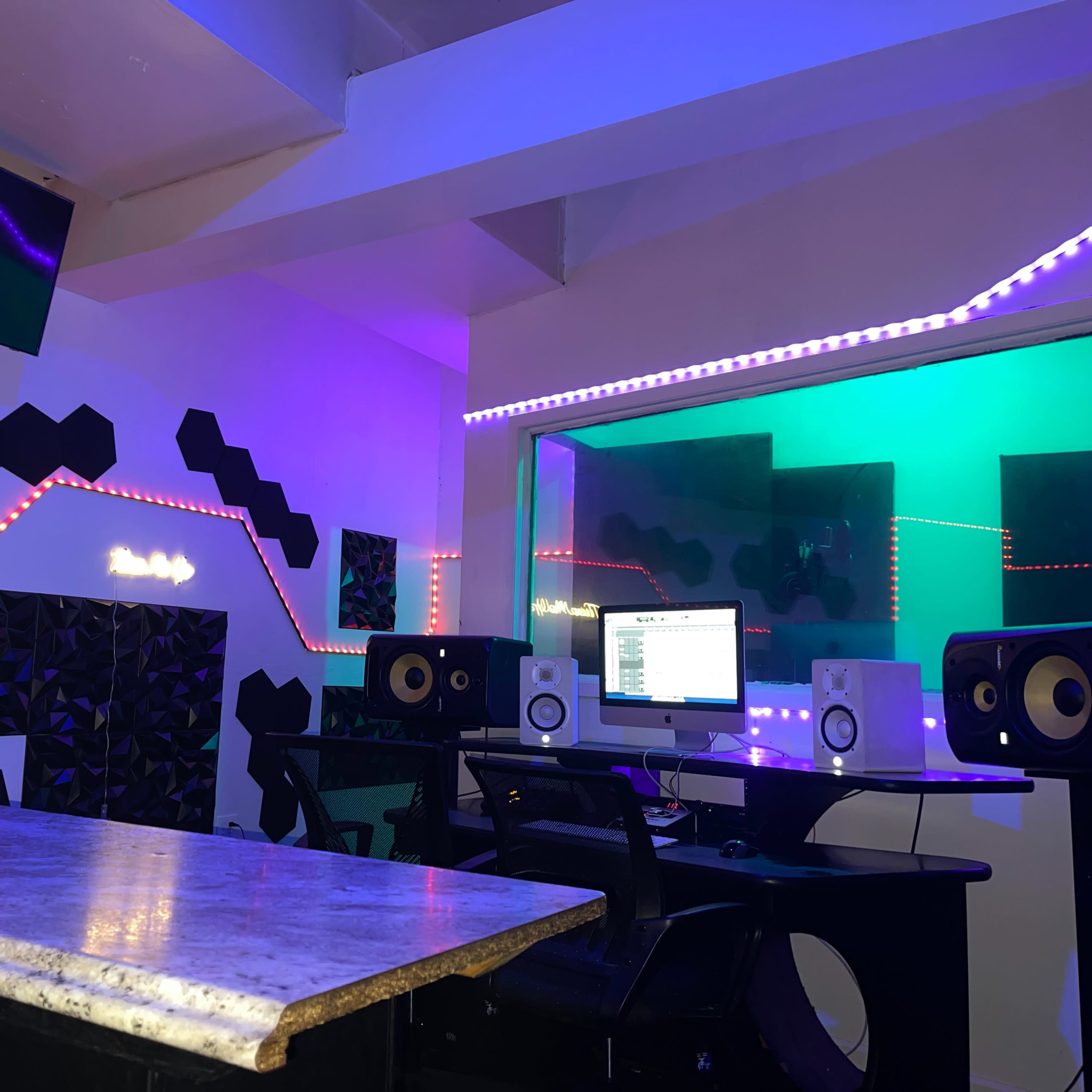 A music studio featuring a computer workstation, speakers, and colorful LED lighting on the walls.
