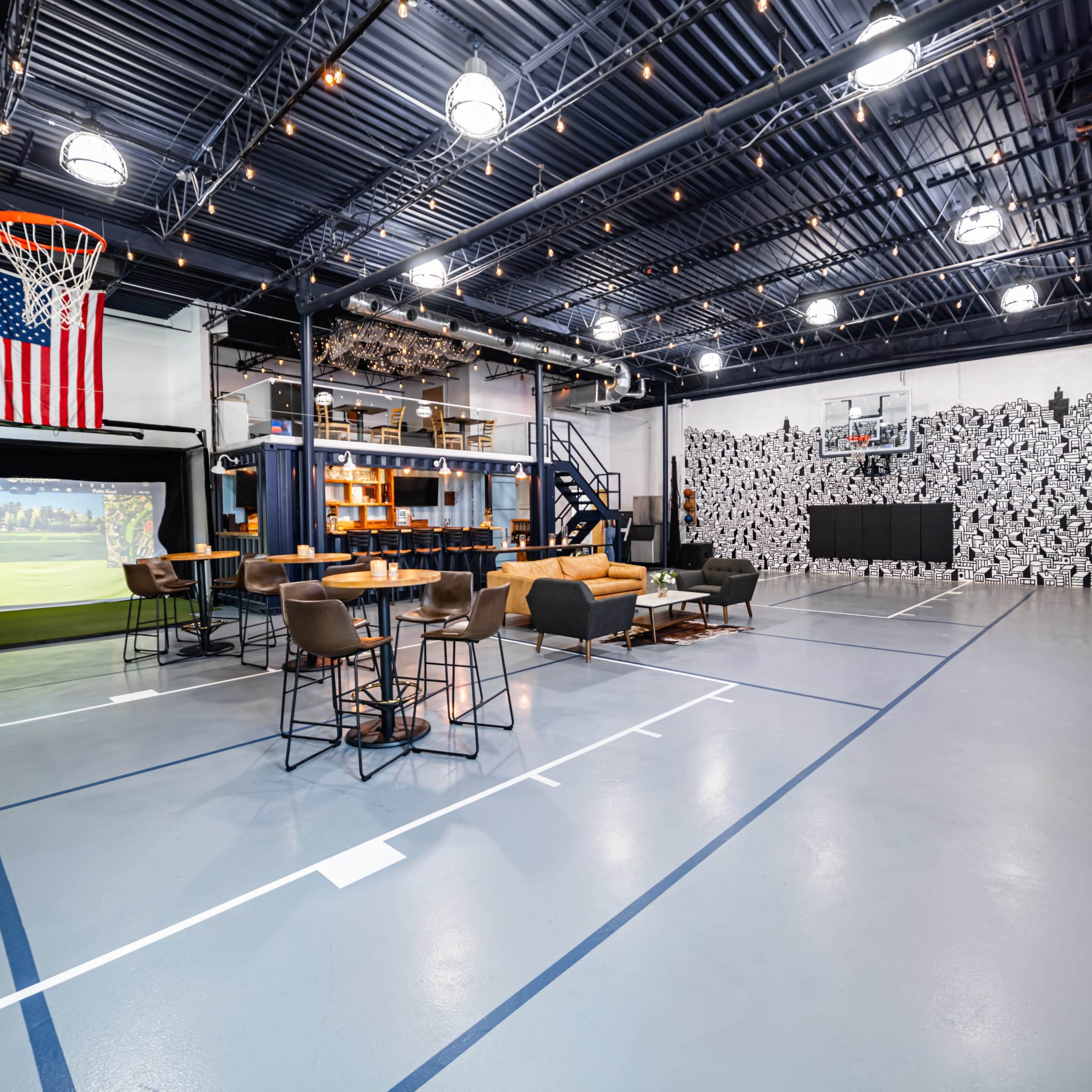A spacious recreational area featuring a basketball hoop, a golf simulator setup, a large TV, seating arrangements, and a decorative wall.