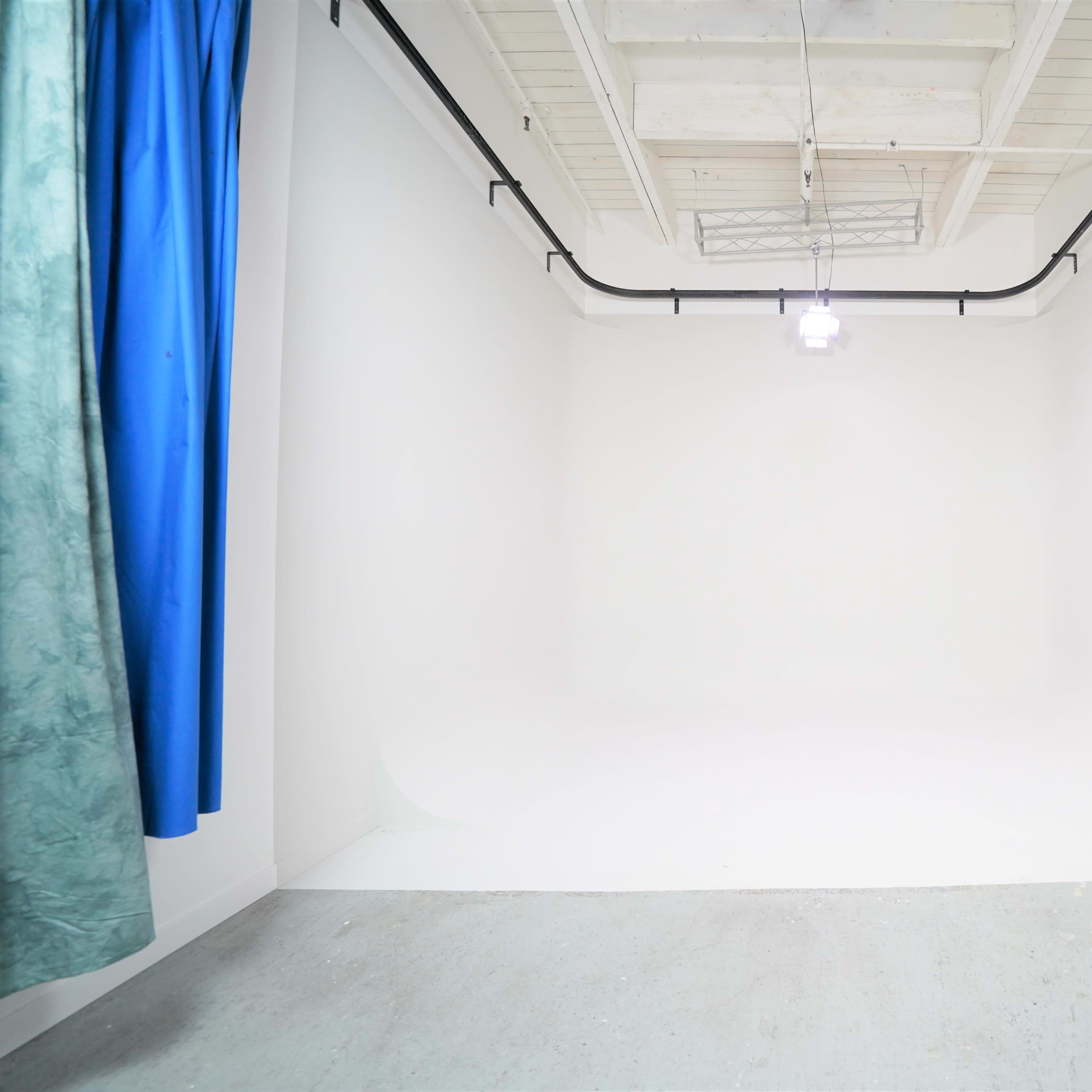 A minimalistic studio space with white walls, a concrete floor, and a single overhead light fixture.