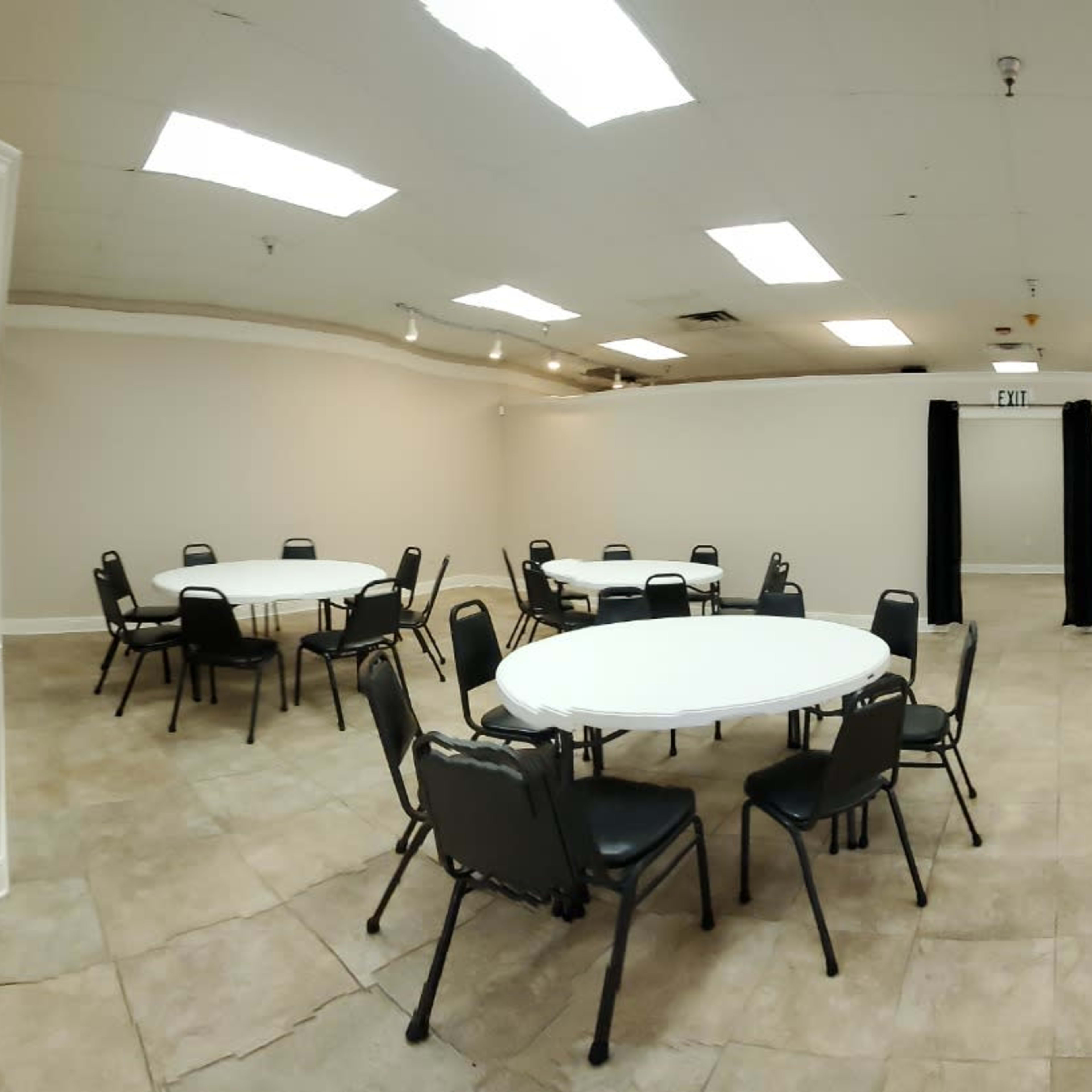 A spacious, well-lit meeting room with several round tables surrounded by chairs, and an entrance visible on the left.
