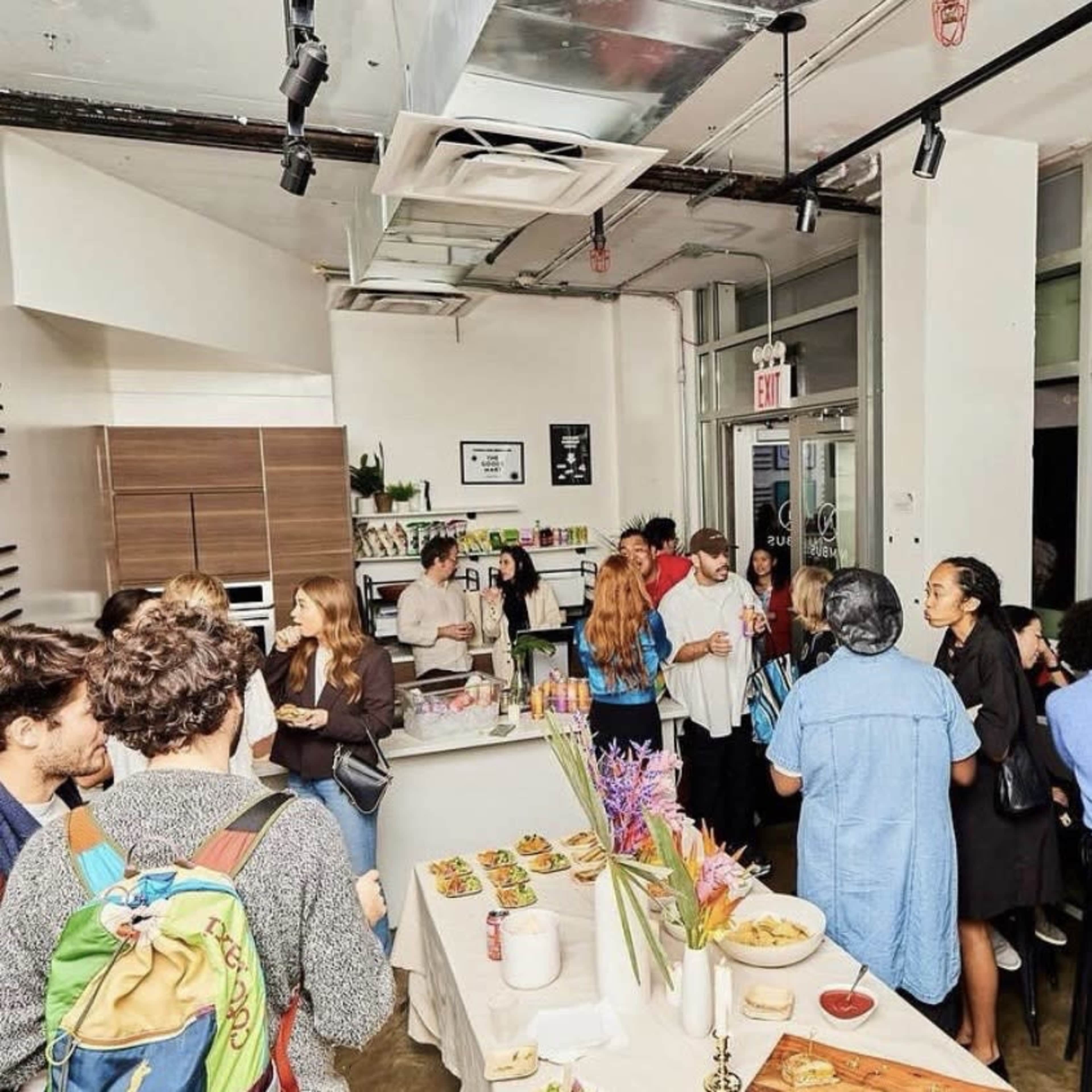 A group of people socialize in a modern kitchen space filled with food and drinks.