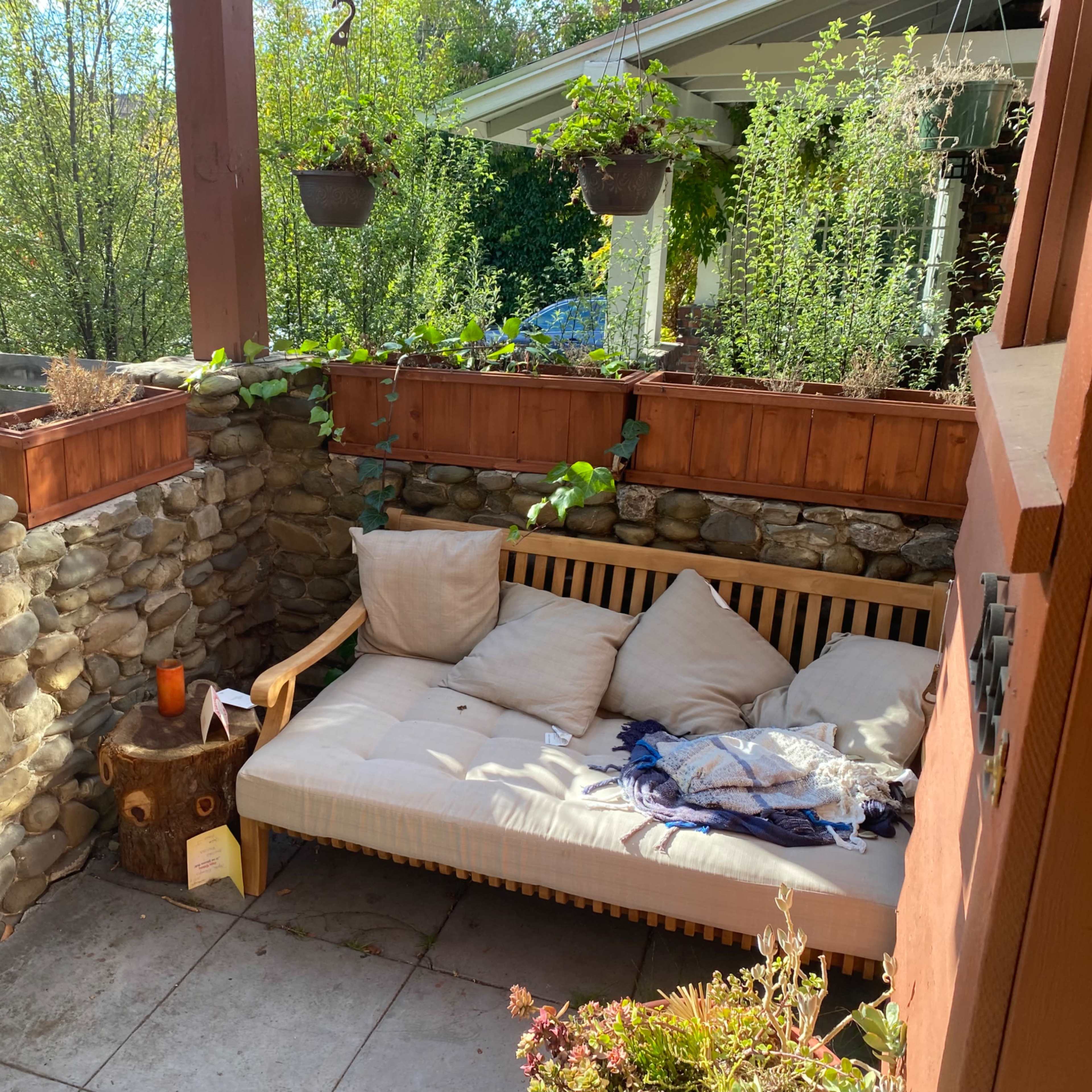 A sheltered outdoor seating area with a wooden couch, stone walls, and potted plants.
