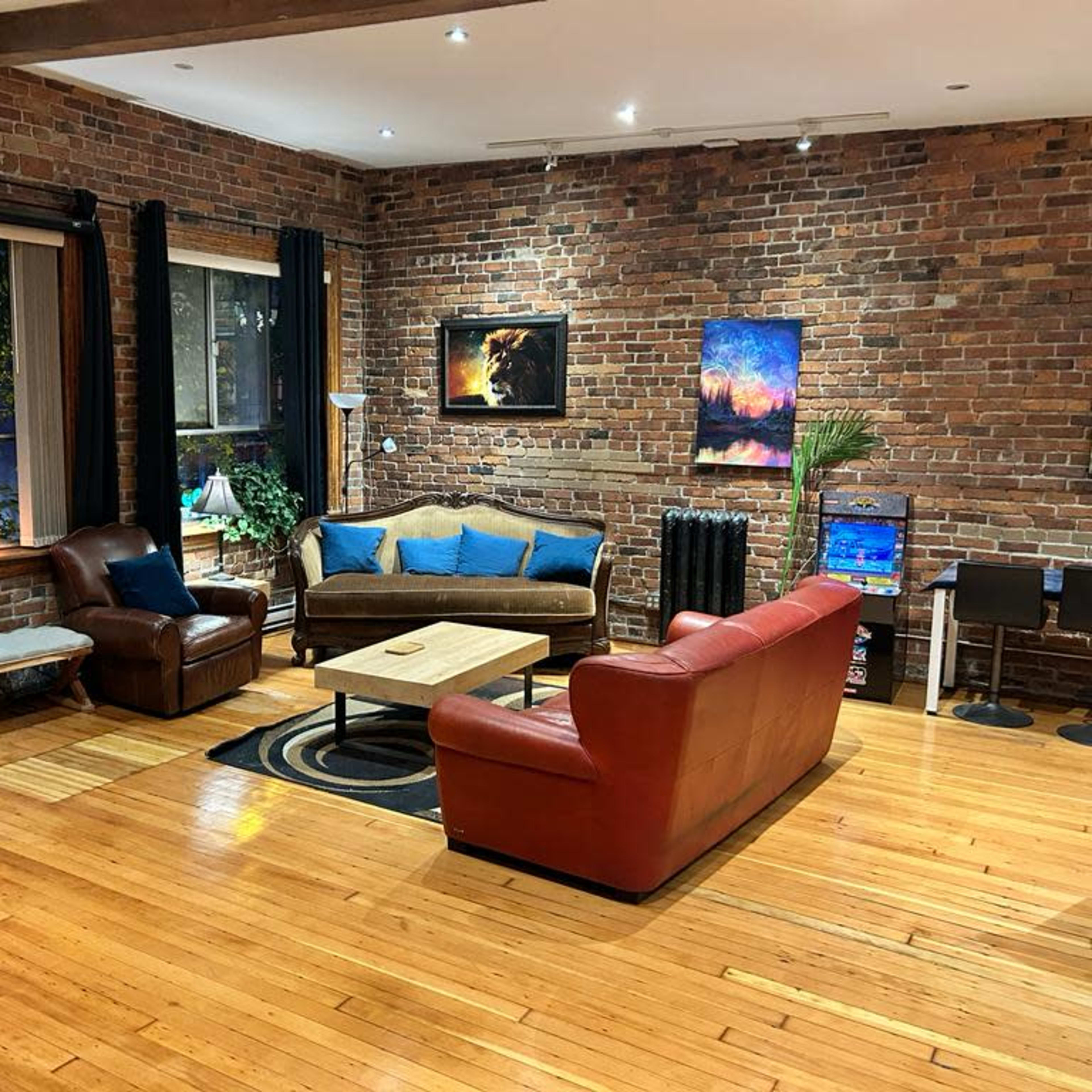A living room with exposed brick walls, hardwood floors, and various seating arrangements including a brown leather chair and a red couch.