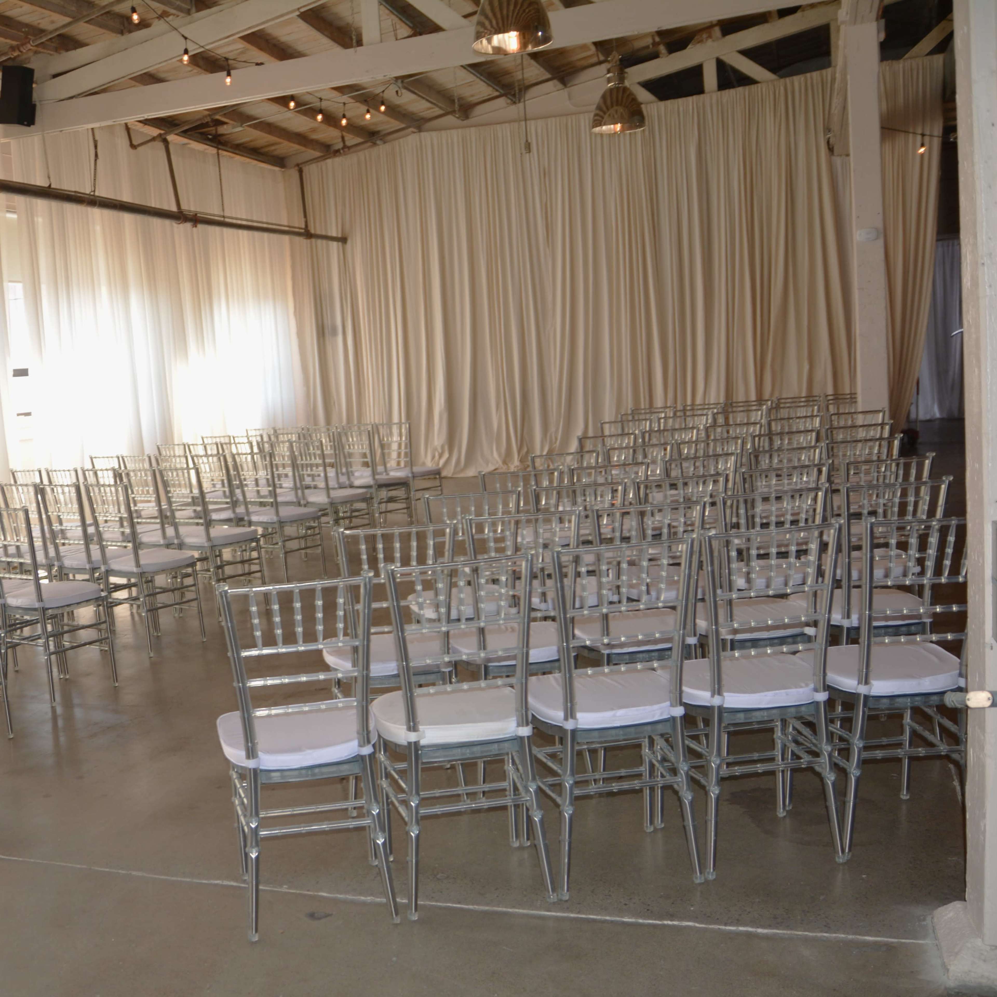 A spacious indoor venue set up with rows of silver chiavari chairs arranged for an event.