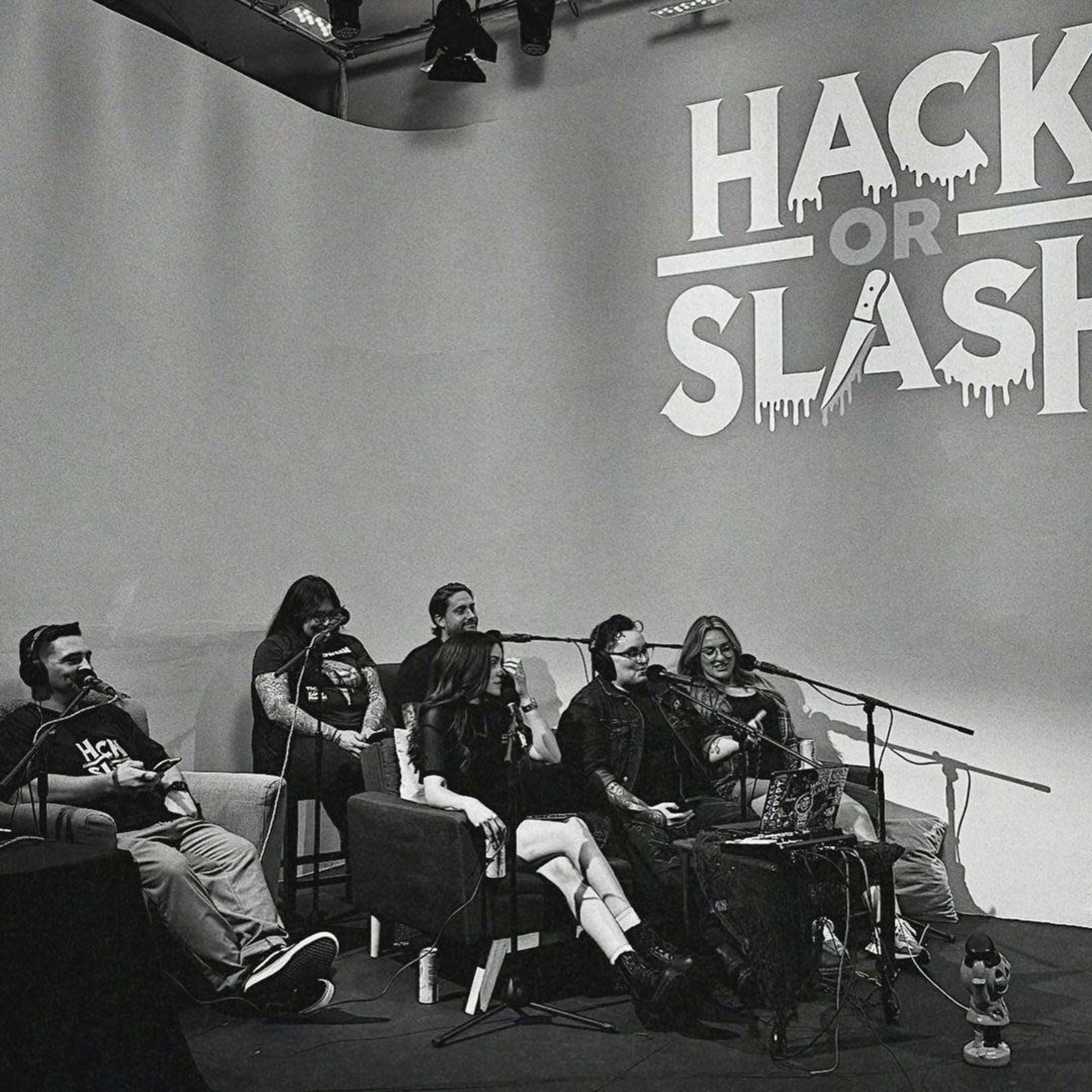 A group of five people sits at a table in front of a large backdrop that reads "HACK OR SLASH," with various microphones and equipment displayed.