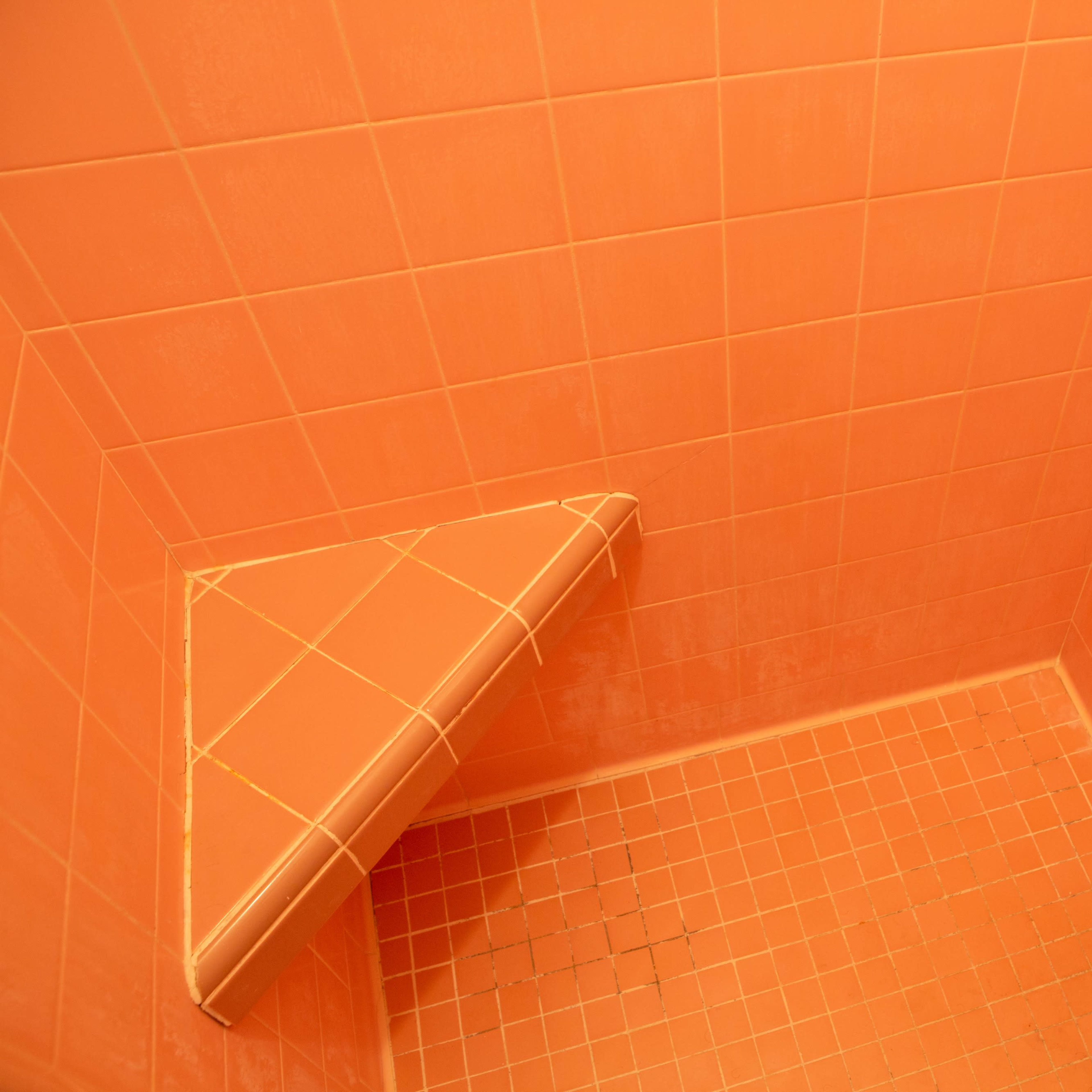 A small, corner shower stall lined with orange tiles.