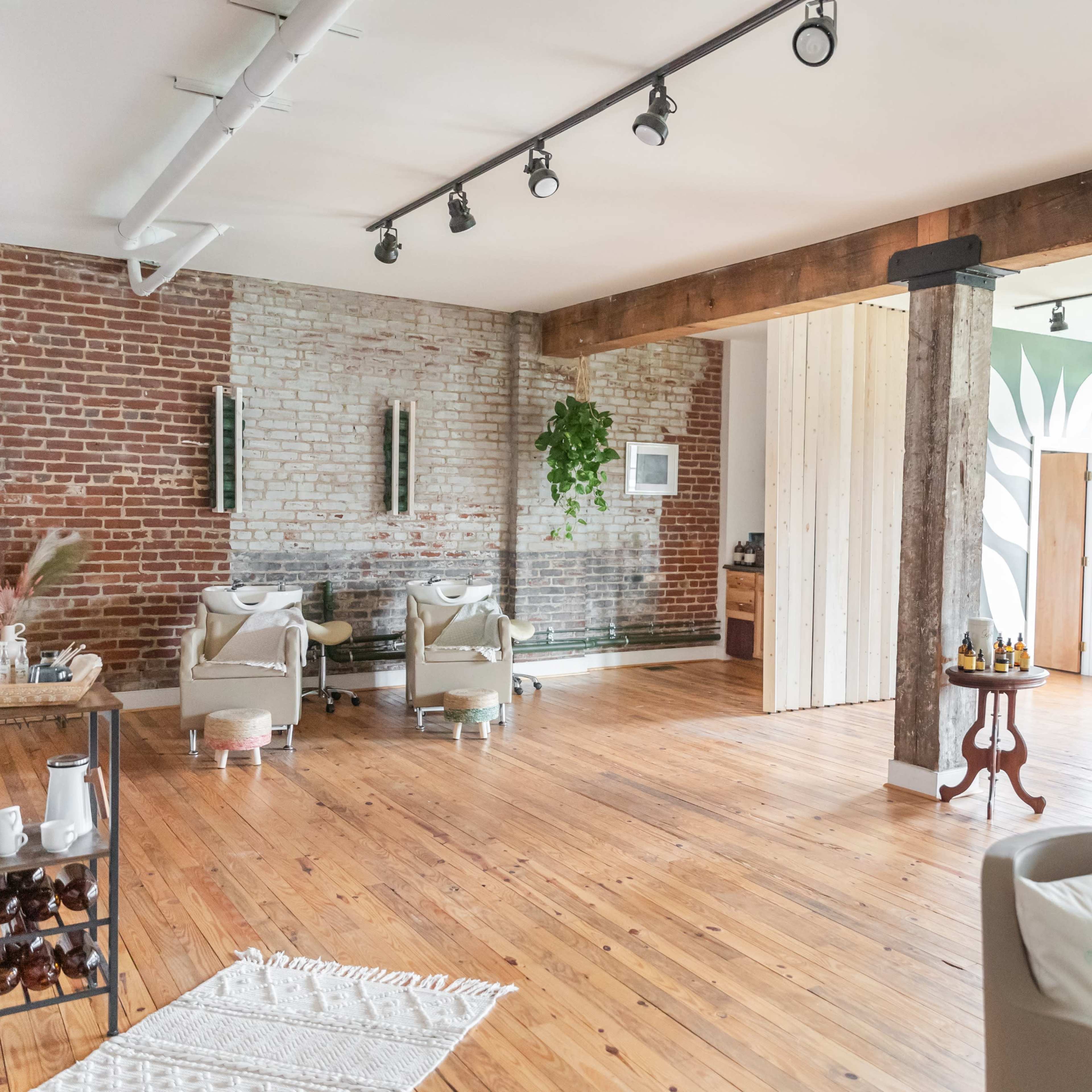 A spacious interior with exposed brick walls, wooden floors, and cozy furniture arranged in a wellness studio.