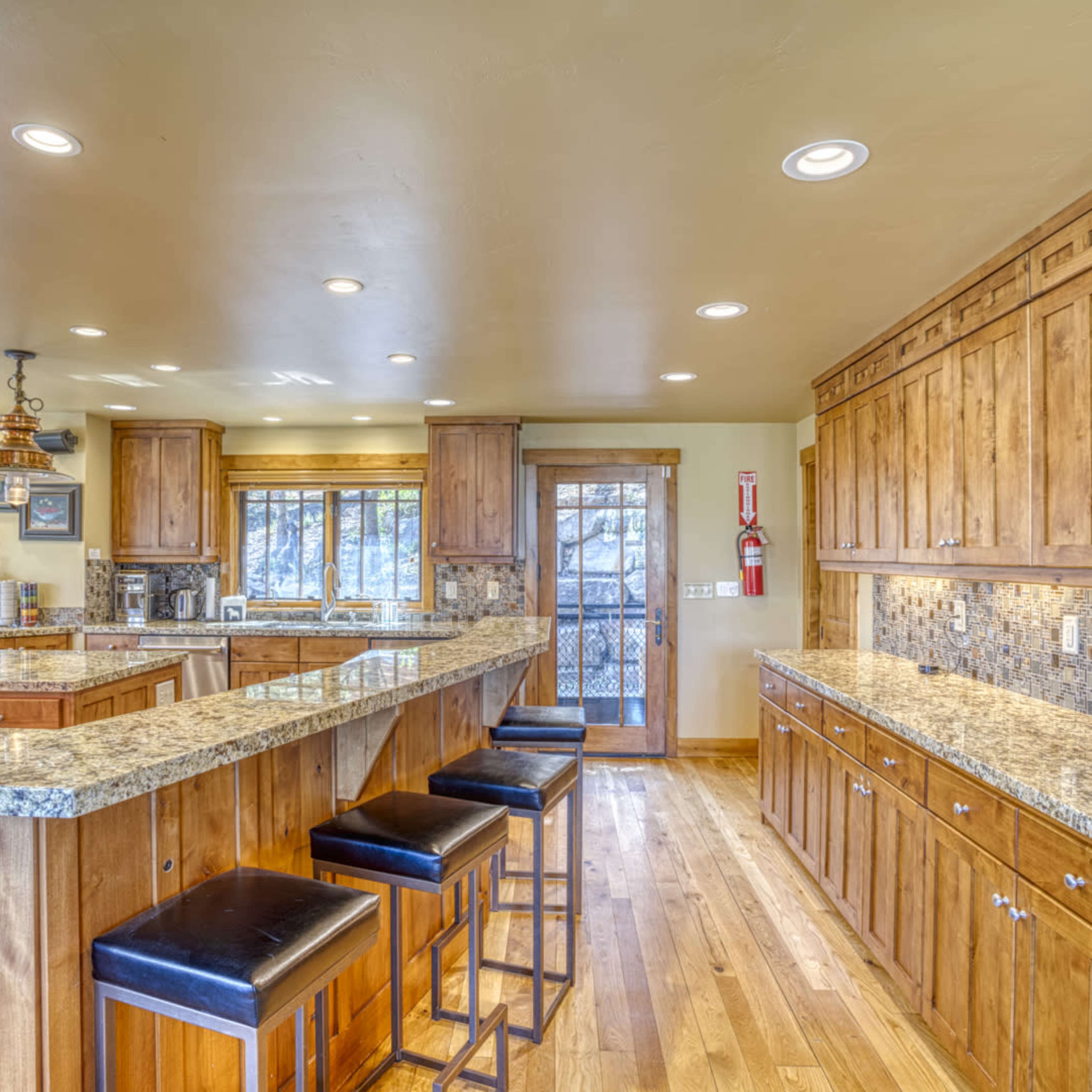 A spacious kitchen with wooden cabinets, granite countertops, and a central island with black bar stools.