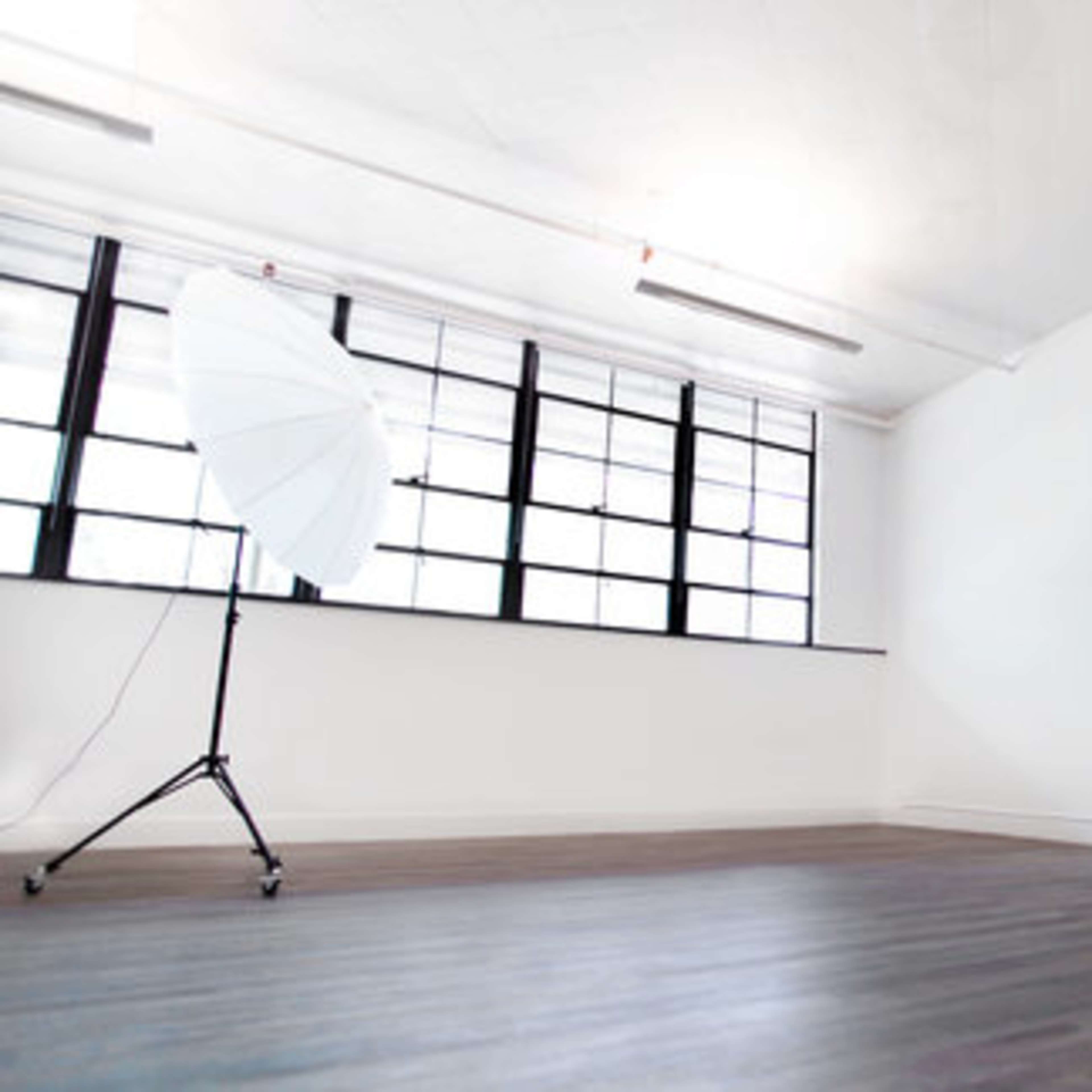 A well-lit photography studio features a large umbrella softbox and a spacious wooden floor.