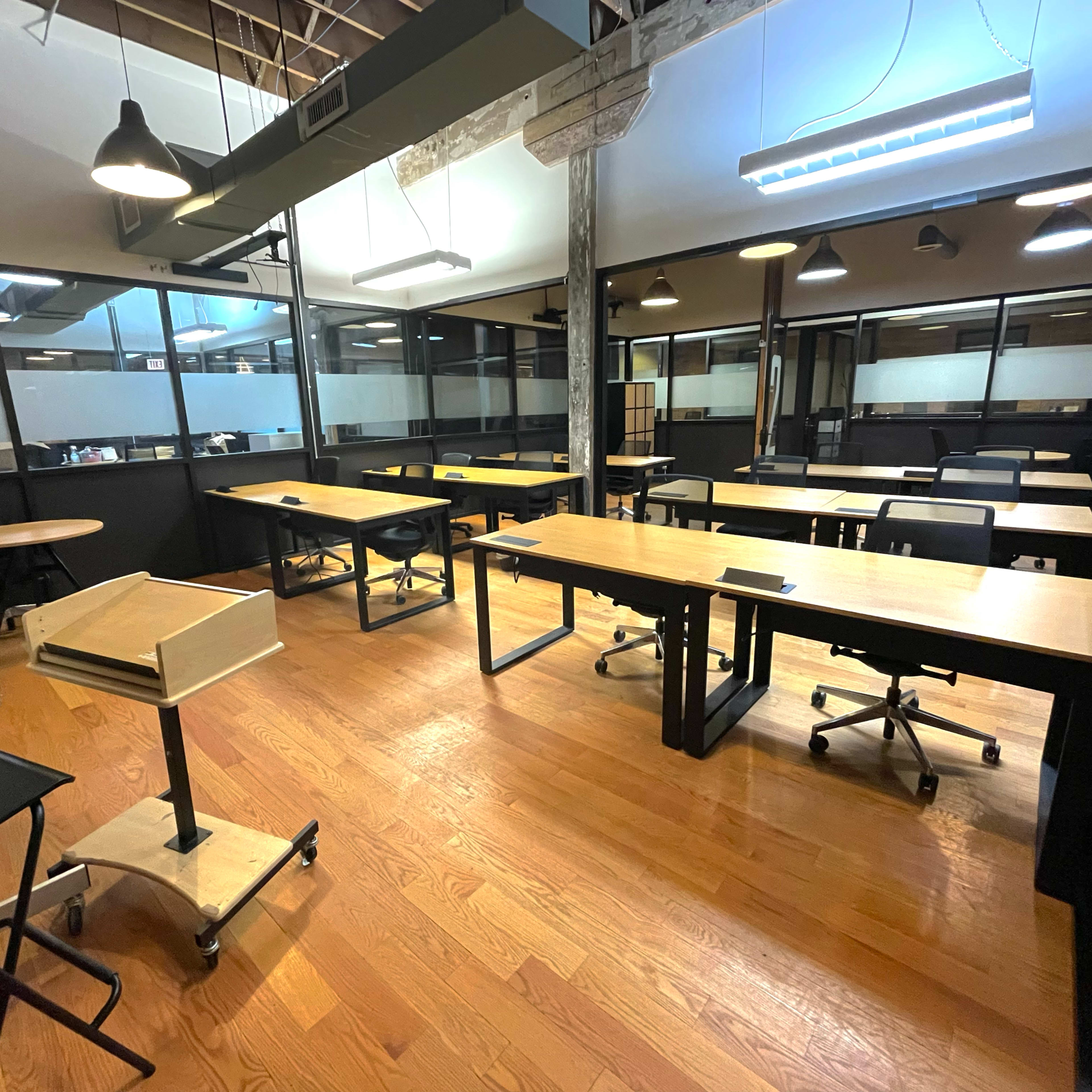 A spacious, well-lit office area with multiple workstations consisting of desks and chairs arranged in an open layout.