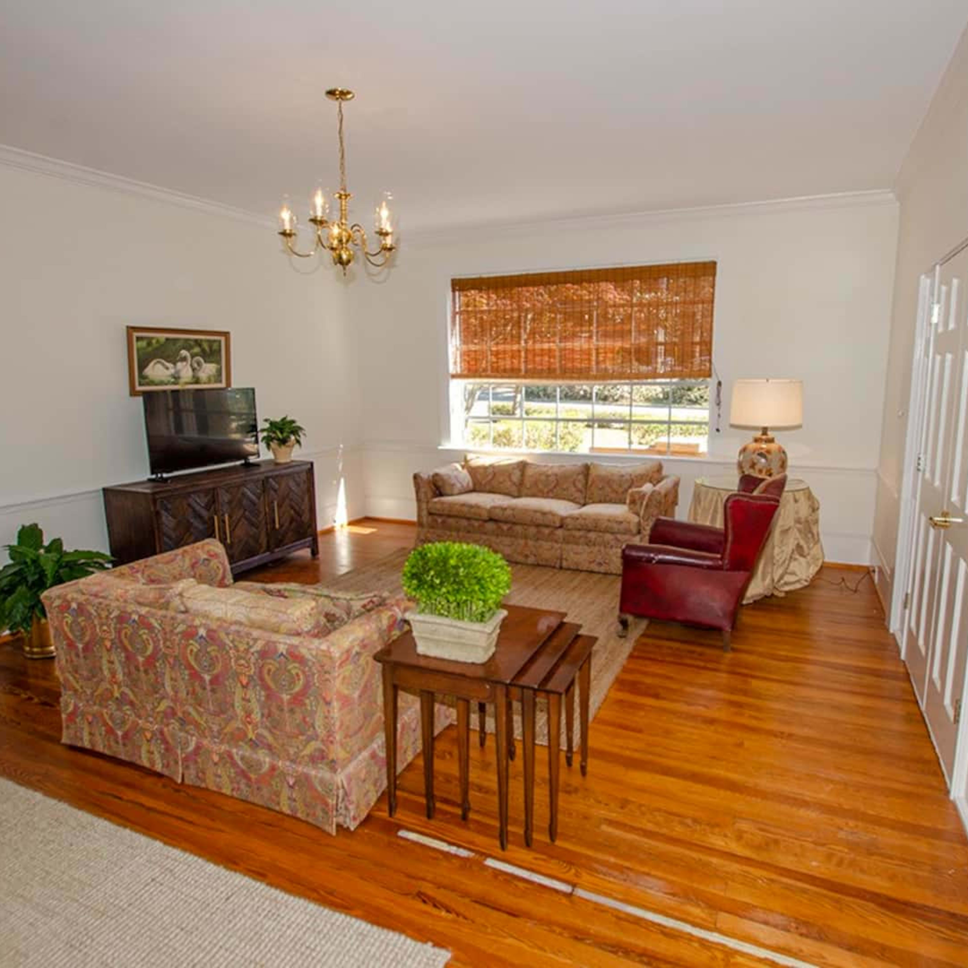 The living room features a television on a cabinet, a sofa set, a table, and a window with natural light.