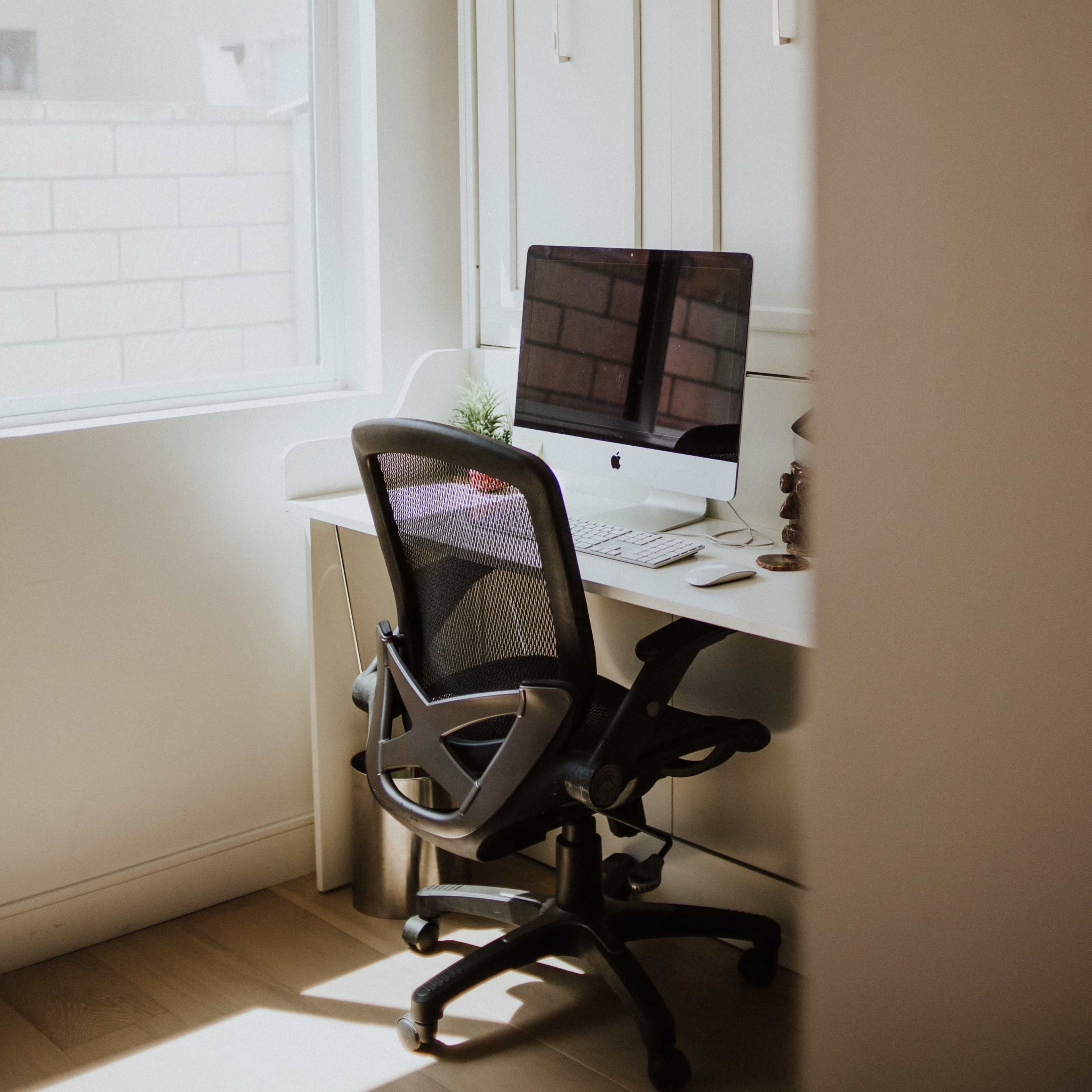 A home office setup with a desk, a computer monitor, and an ergonomic chair positioned near a window.