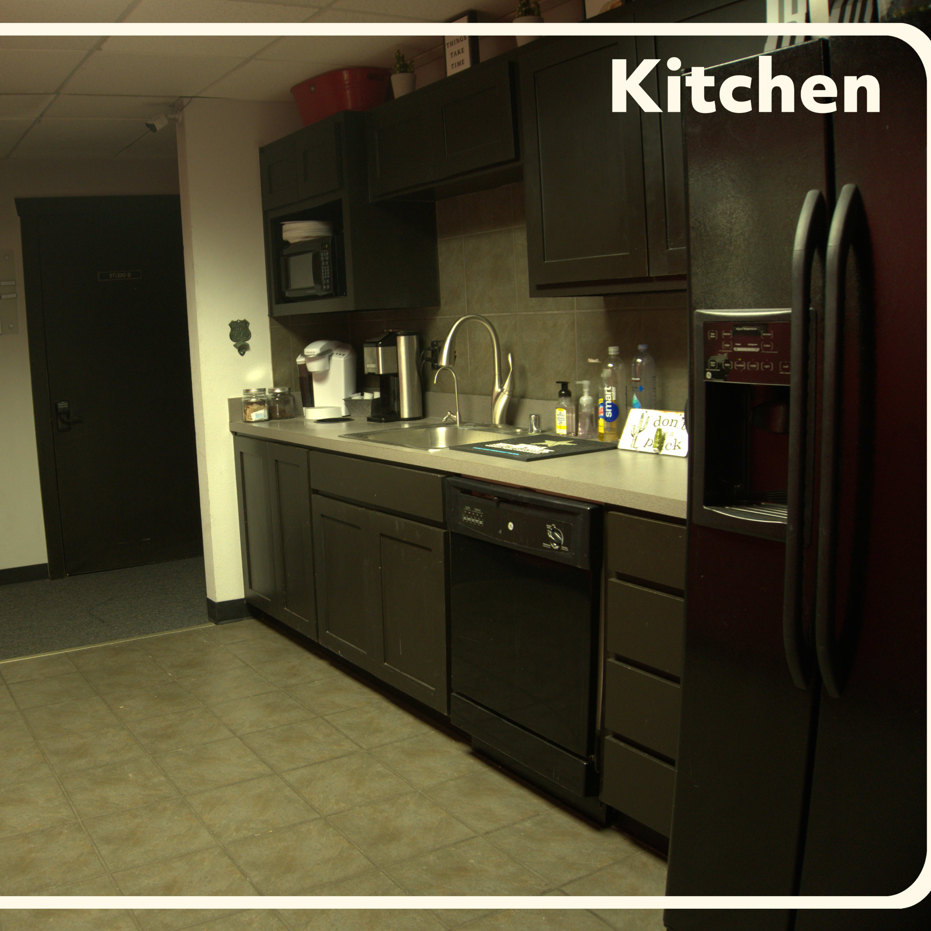 A kitchenette with dark cabinetry, a sink, and appliances, set against a partially red wall.