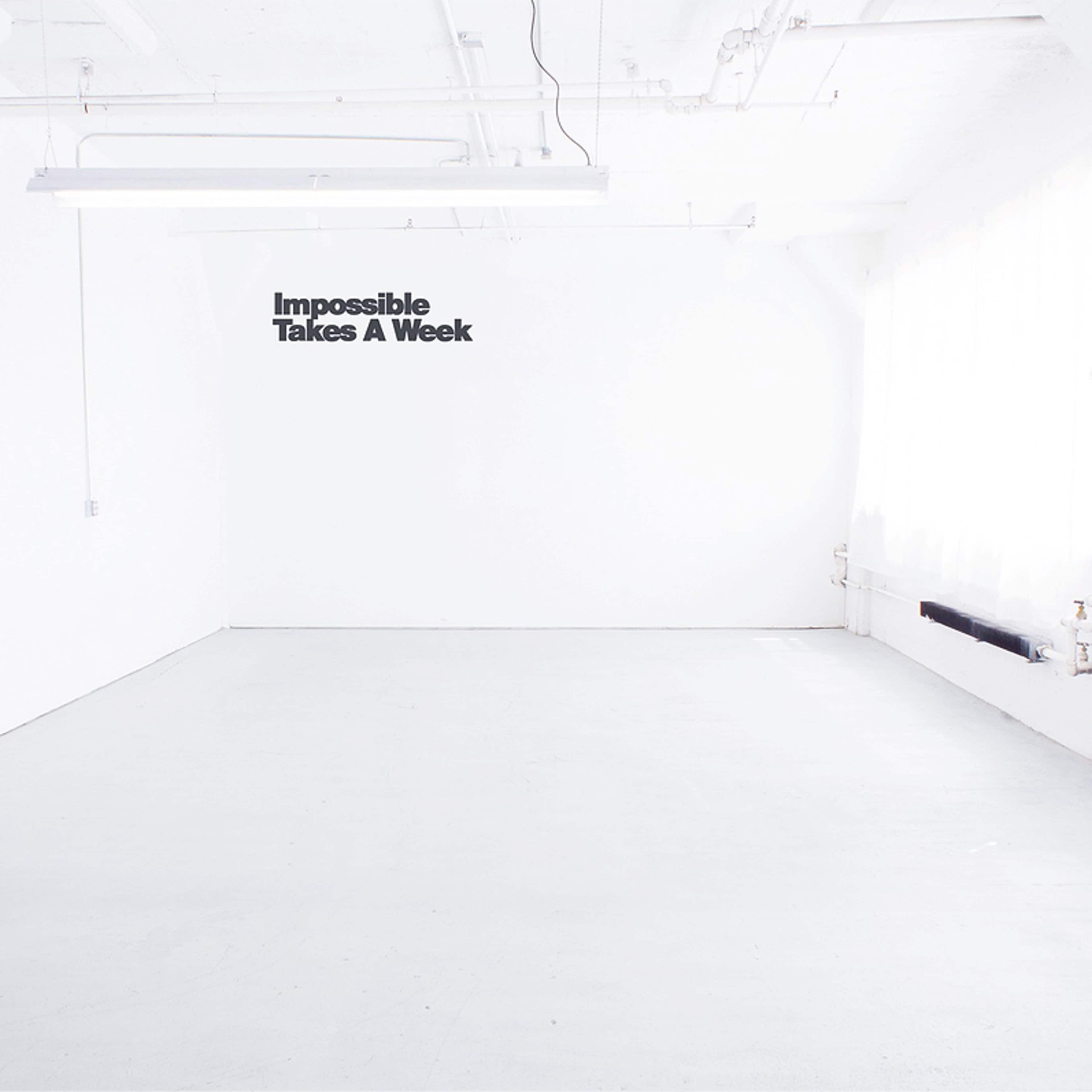A spacious, empty room with white walls, a light-colored floor, and a quote on the wall that reads "Impossible Takes A Week."