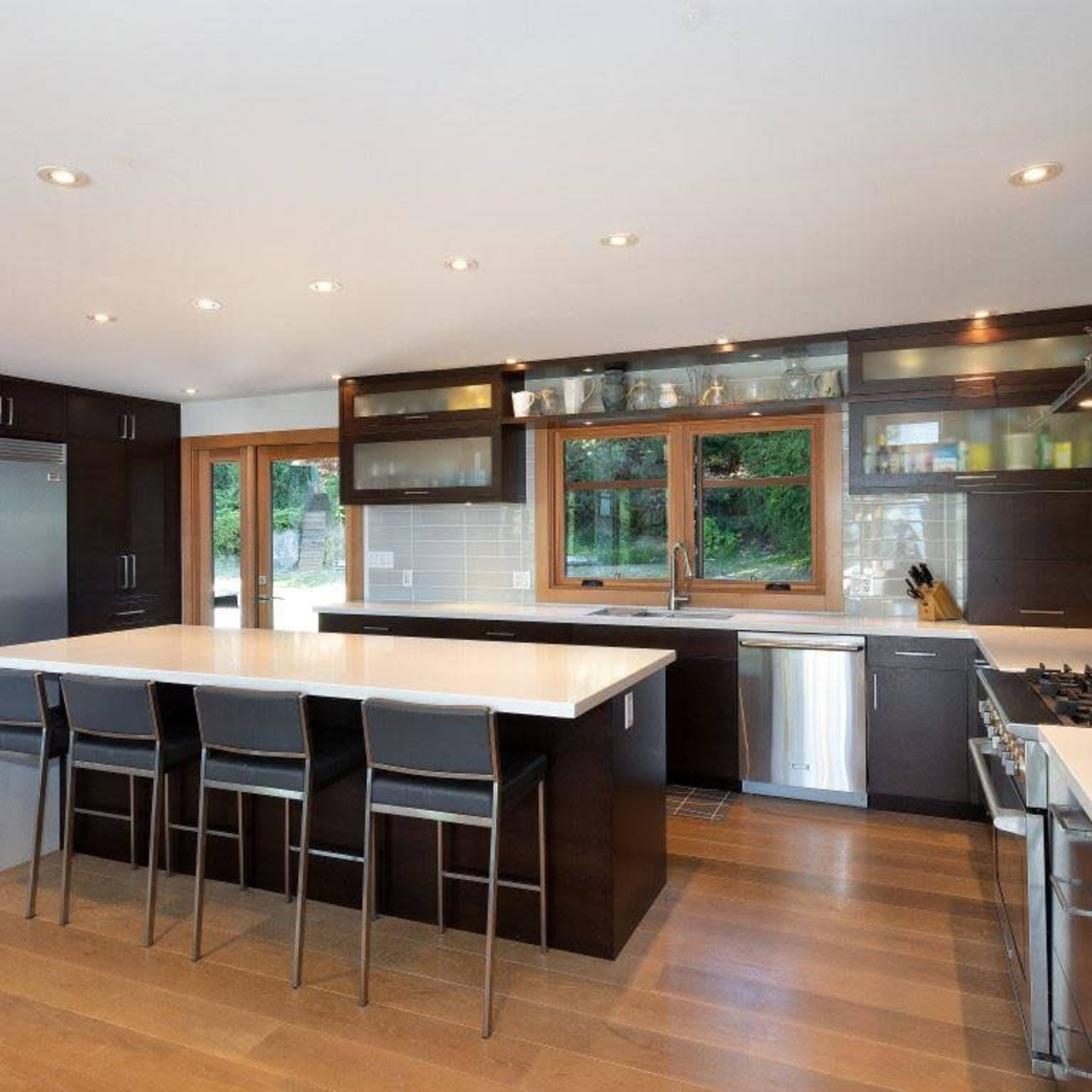 A modern kitchen features dark cabinetry, a large central island with bar seating, and stainless steel appliances.